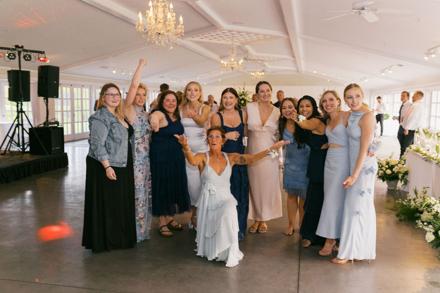 Wedding guests gather on the dance floor under a chandelier during reception celebrations.