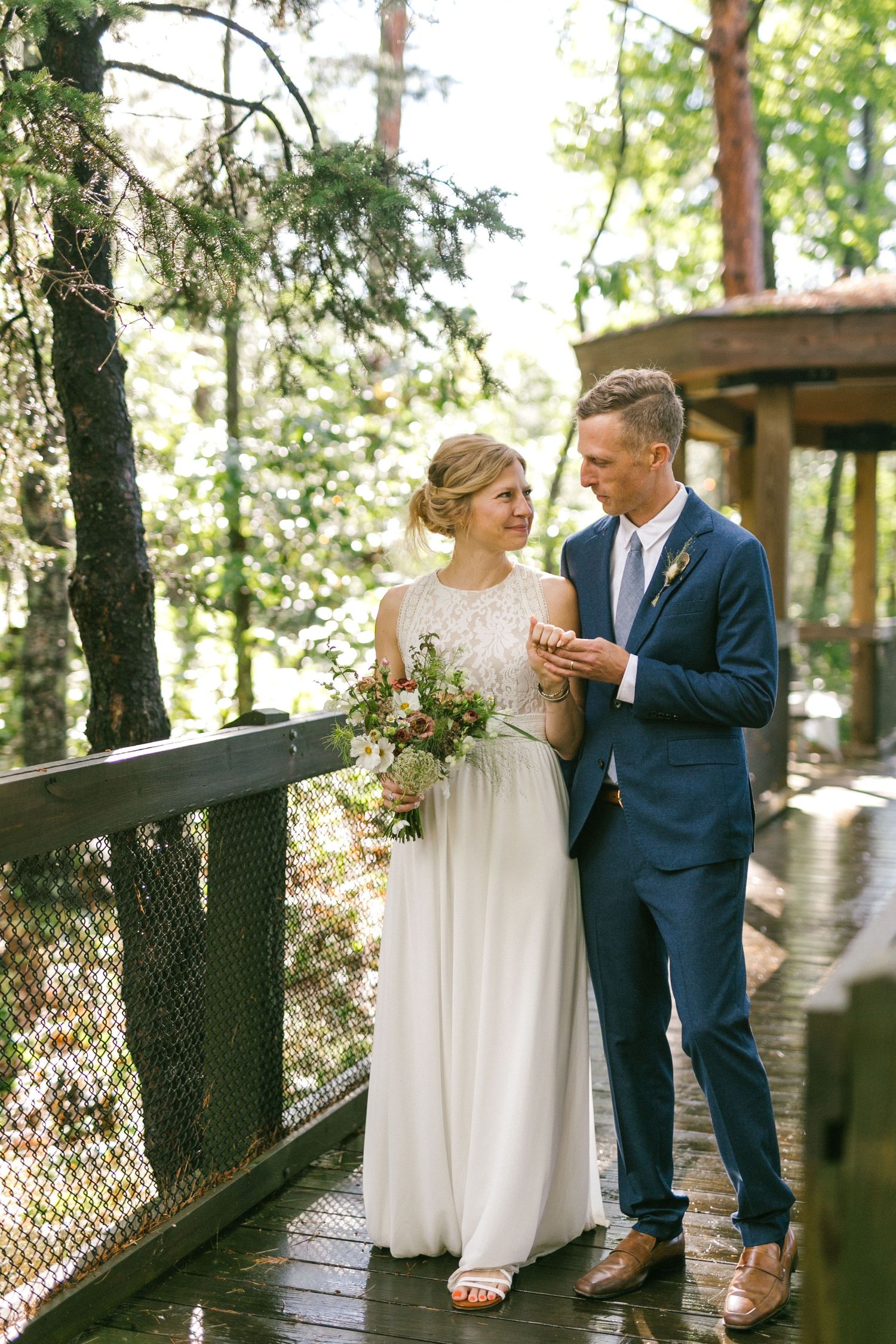 A romantic moment on a wooden deck surrounded by trees as newlyweds share an intimate conversation and wildflower bouquet.