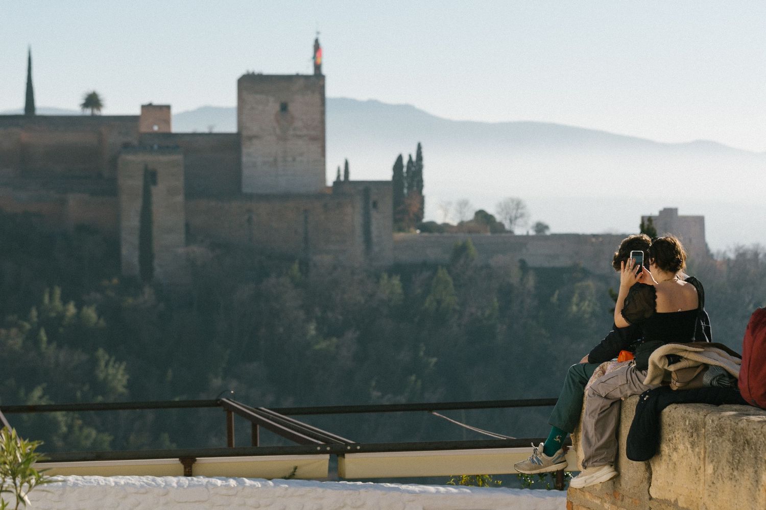 Couple admiring the historic Alhambra palace in Granada, Spain on a misty morning from a scenic overlook.