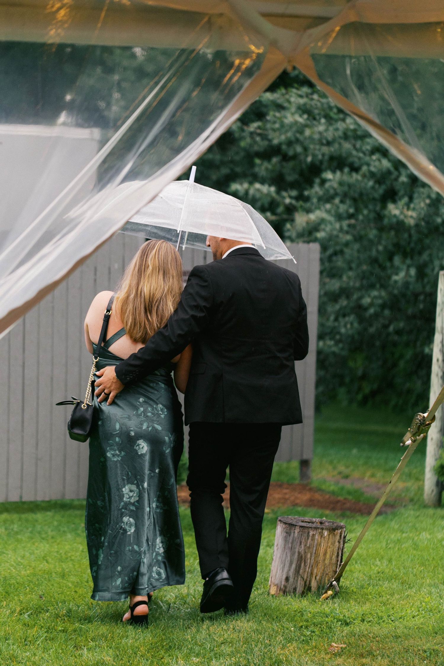 A couple shares an intimate moment under a white canopy tent on a grassy lawn during an outdoor event.