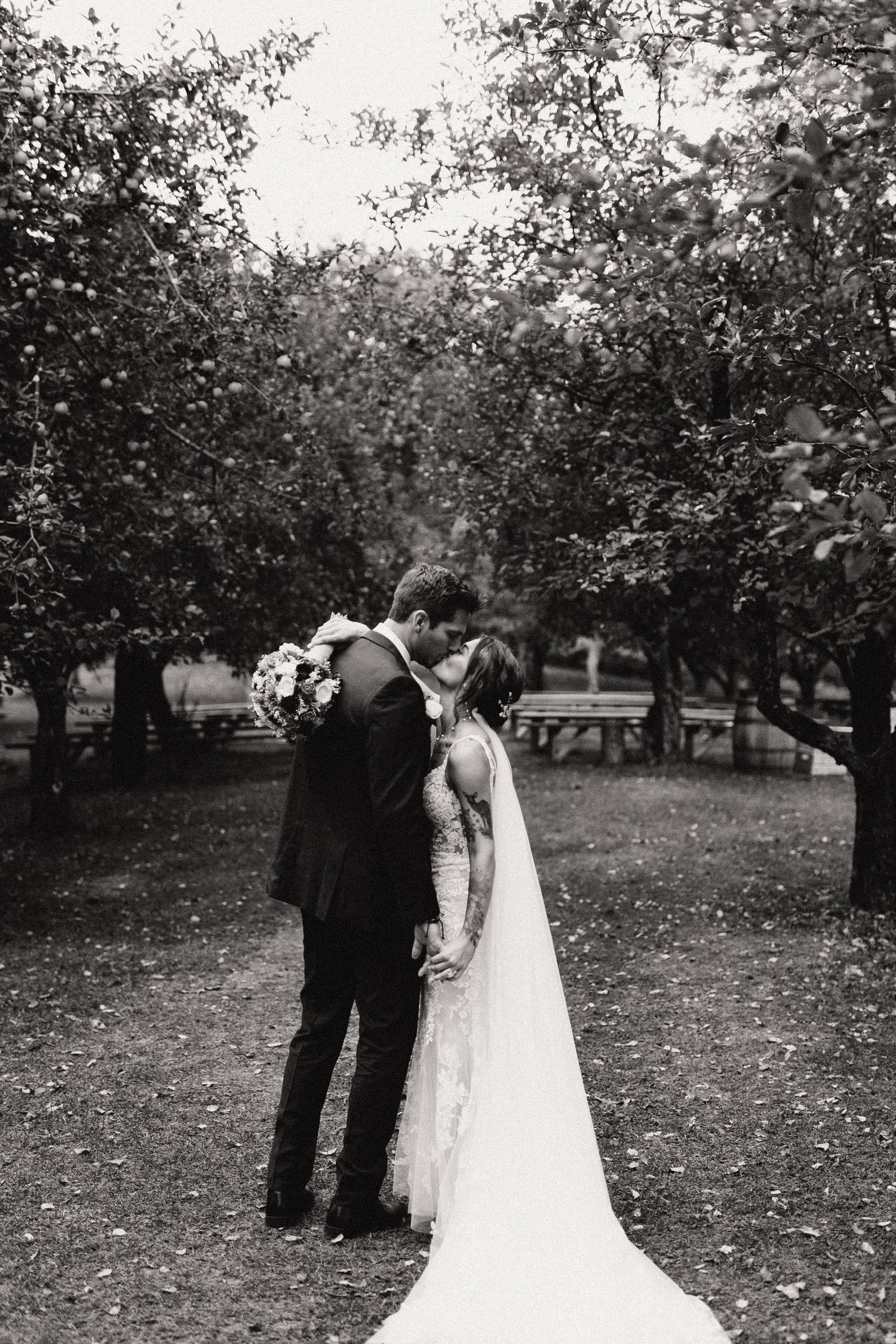 A black and white wedding photo of a couple sharing an intimate moment in an orchard setting.