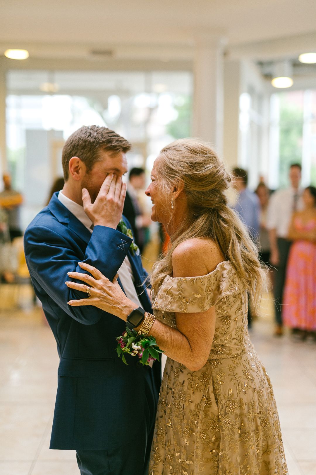 A couple shares an emotional dance moment in formal attire at an indoor venue.