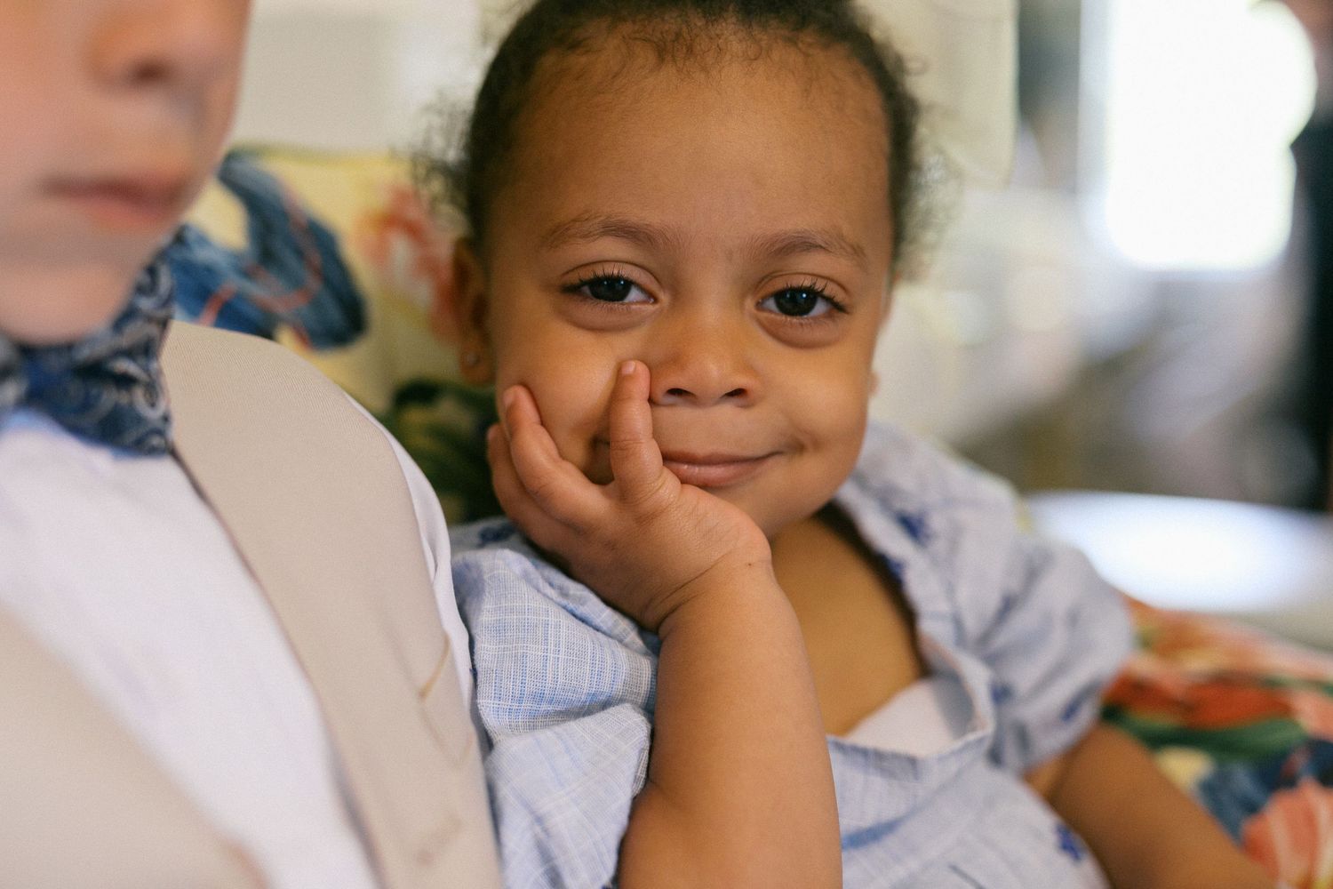 Child smiling and resting head on hand in casual setting.