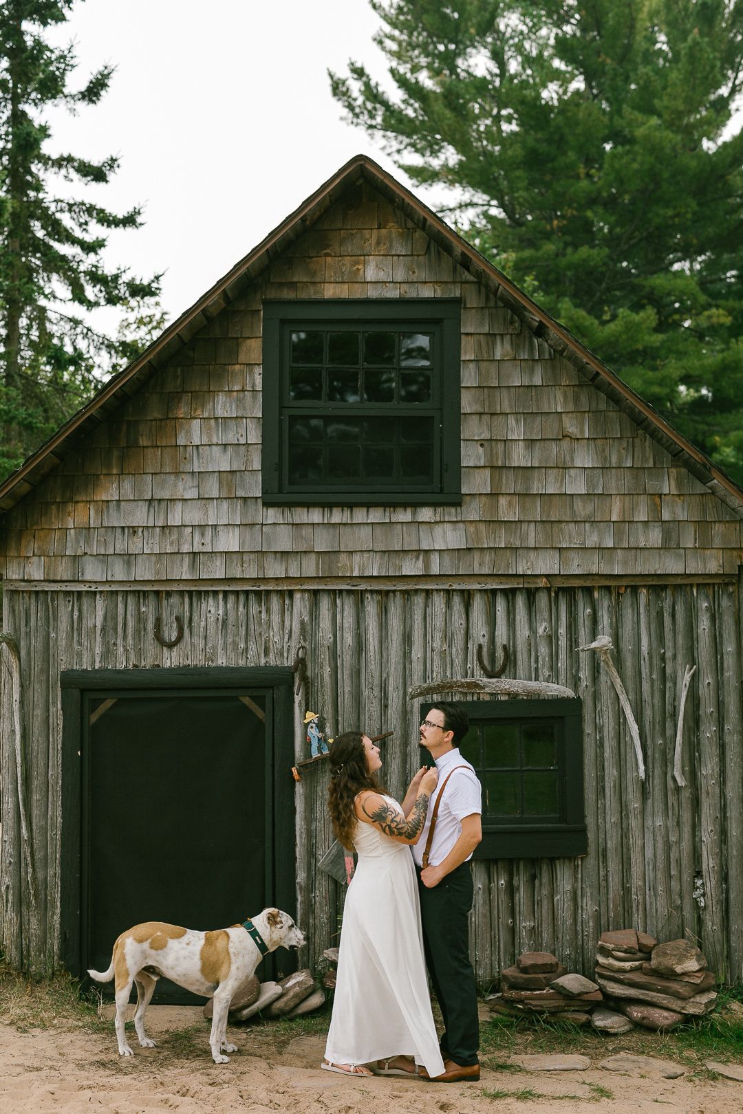 A rustic wooden barn with weathered shingles and a dog resting outside.