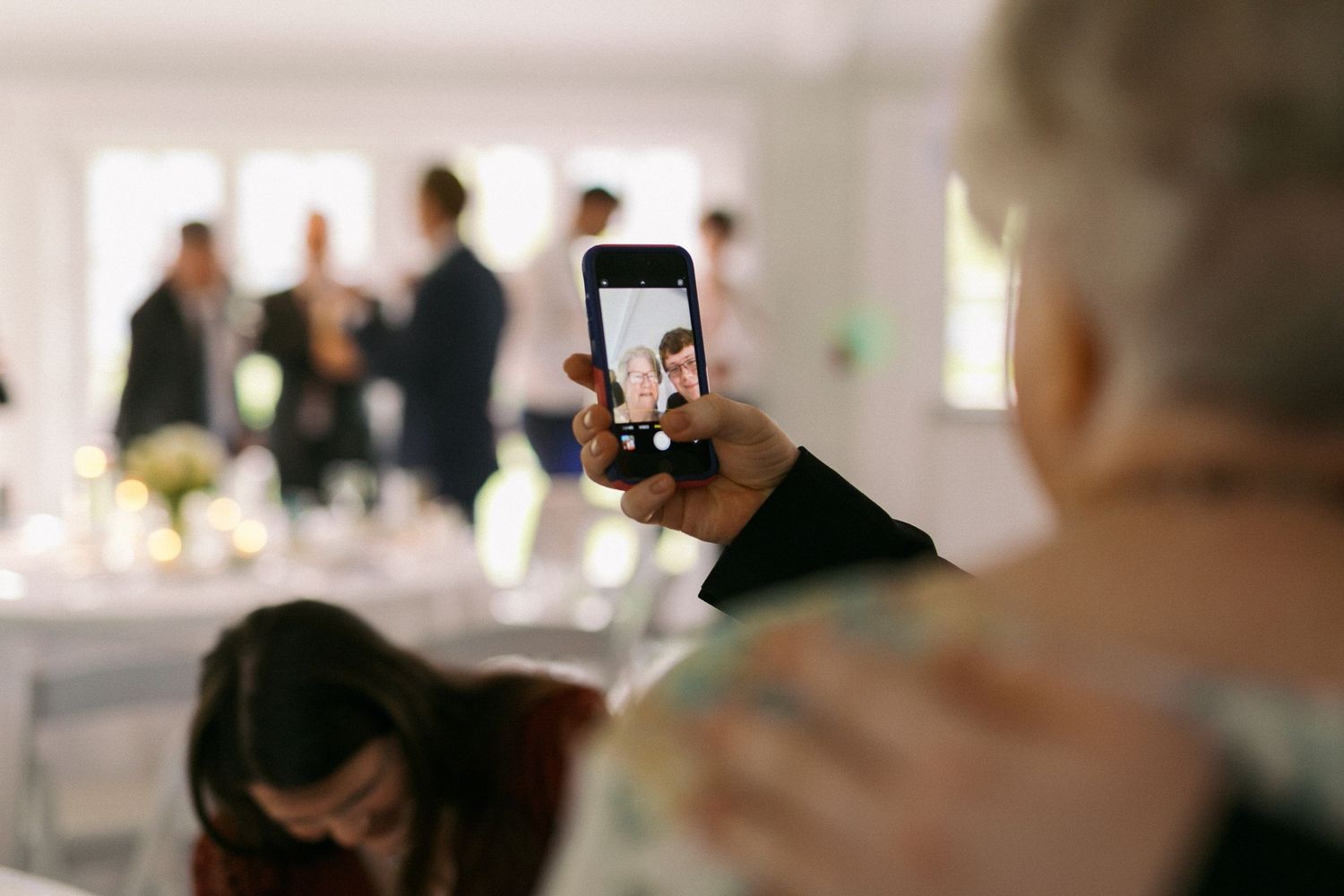 A hand holds up a phone to capture photos at a wedding reception.
