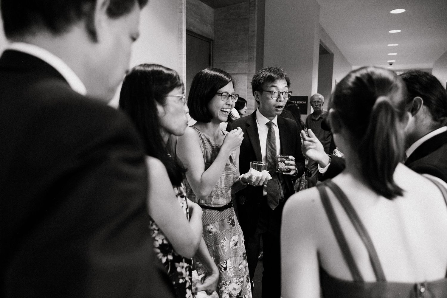 Wedding guests mingle and socialize in black and white candid photo at elegant reception venue.