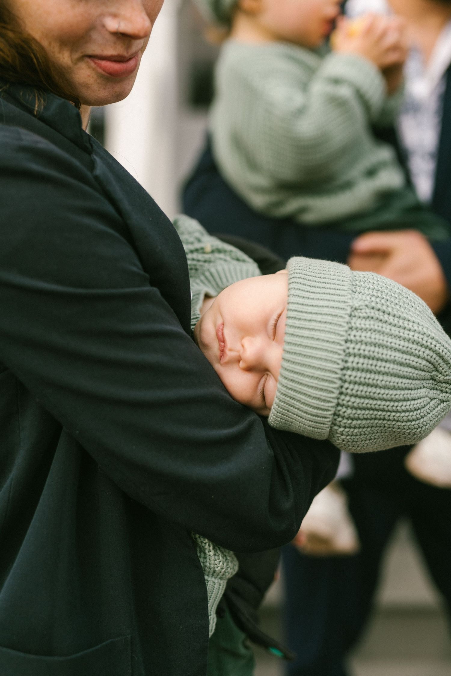 A close-up shot of someone wearing a black sweatshirt holding a baby in a gray knit beanie.