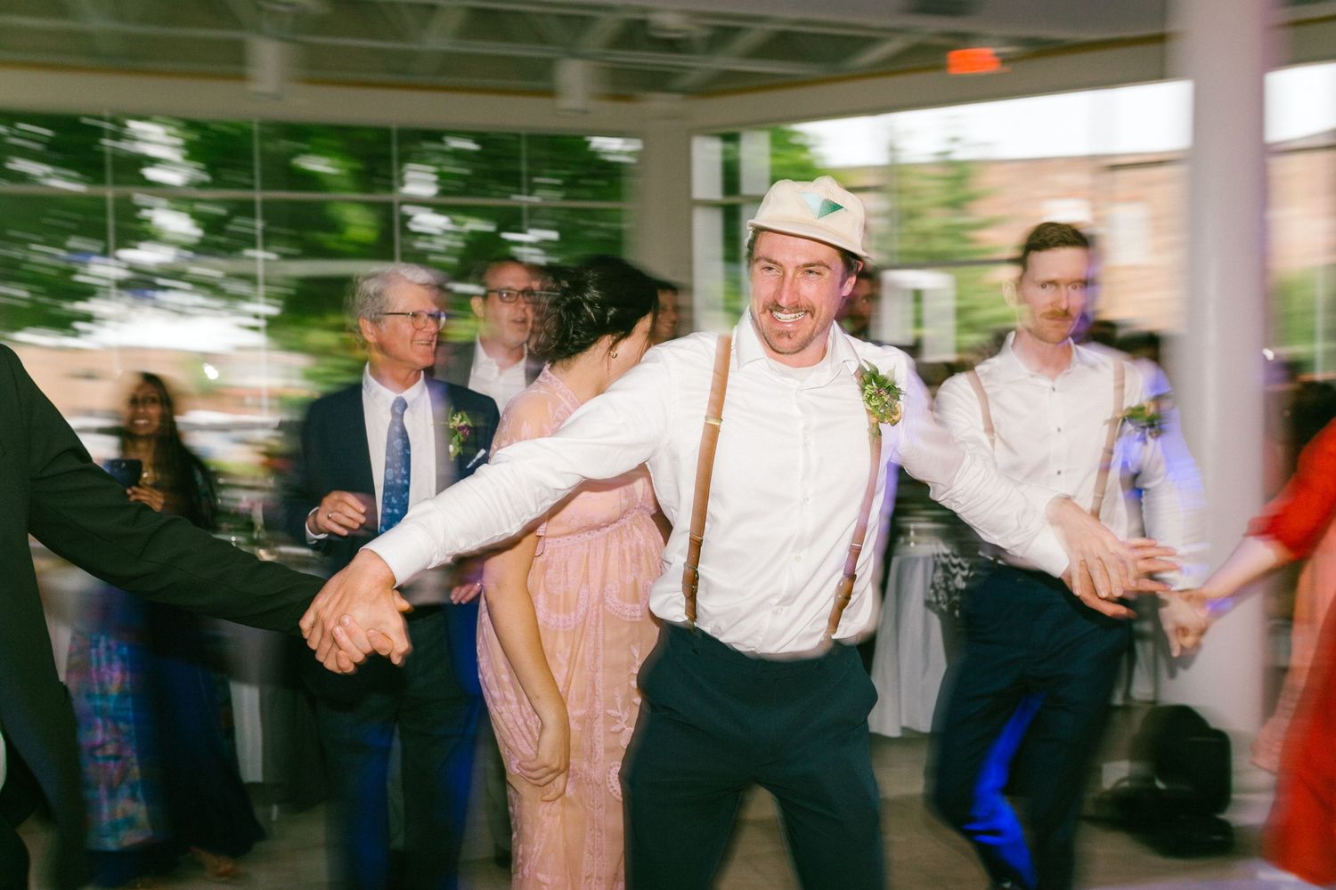 A groom in suspenders dances playfully at a wedding reception.