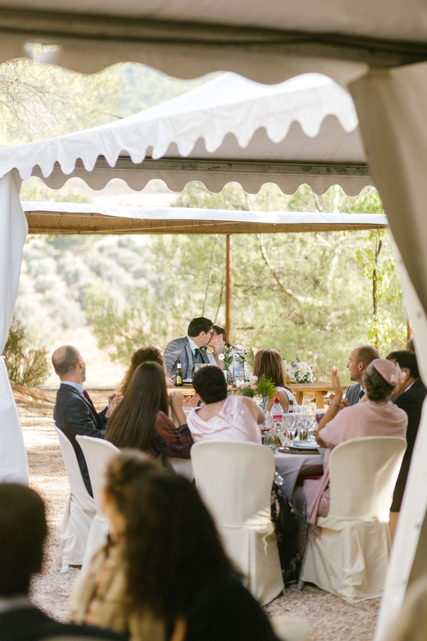 Guests seated under an elegant outdoor canopy enjoying a formal dining event in a natural garden setting.