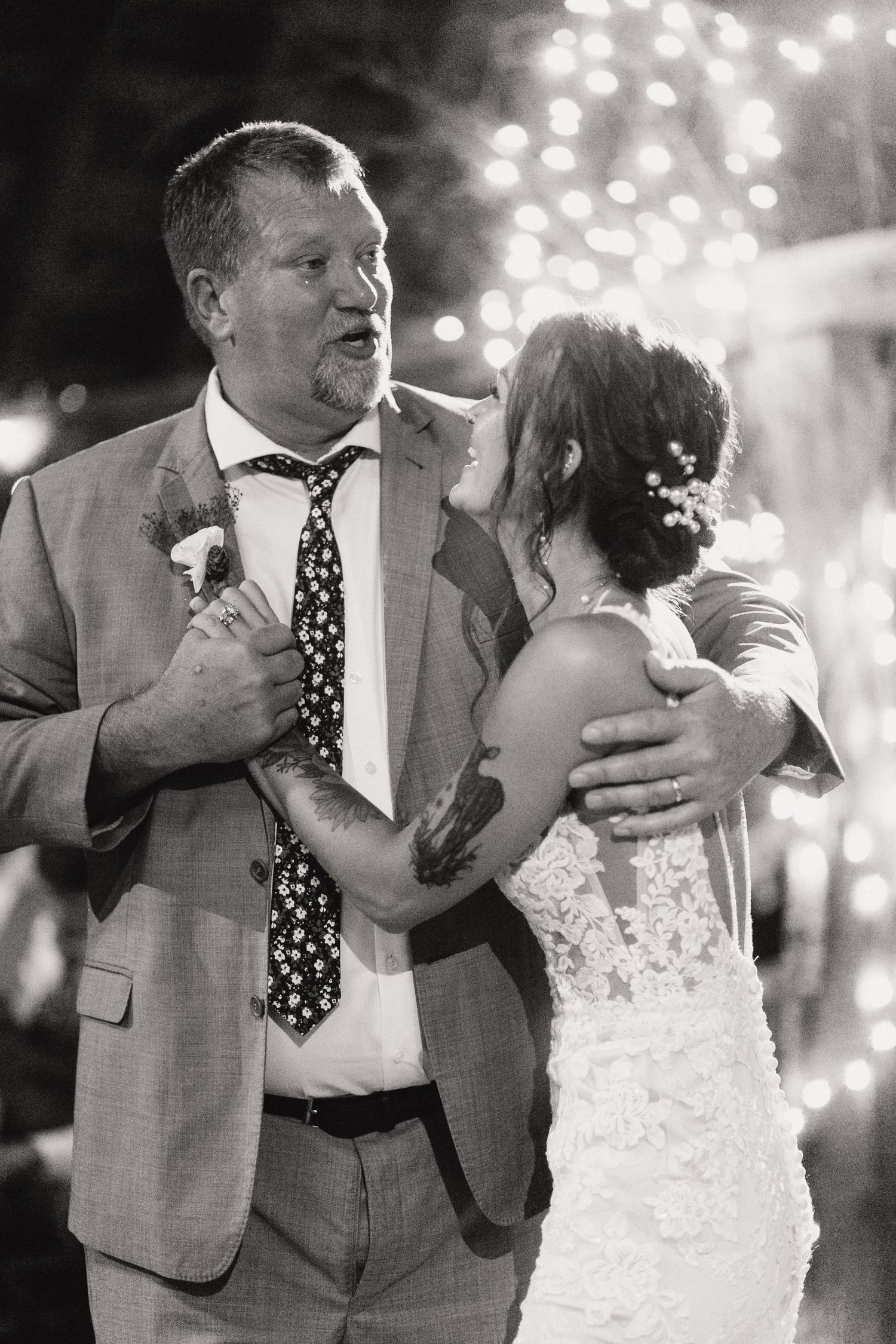 A father and daughter dance moment captured in black and white under sparkling string lights at a wedding reception.