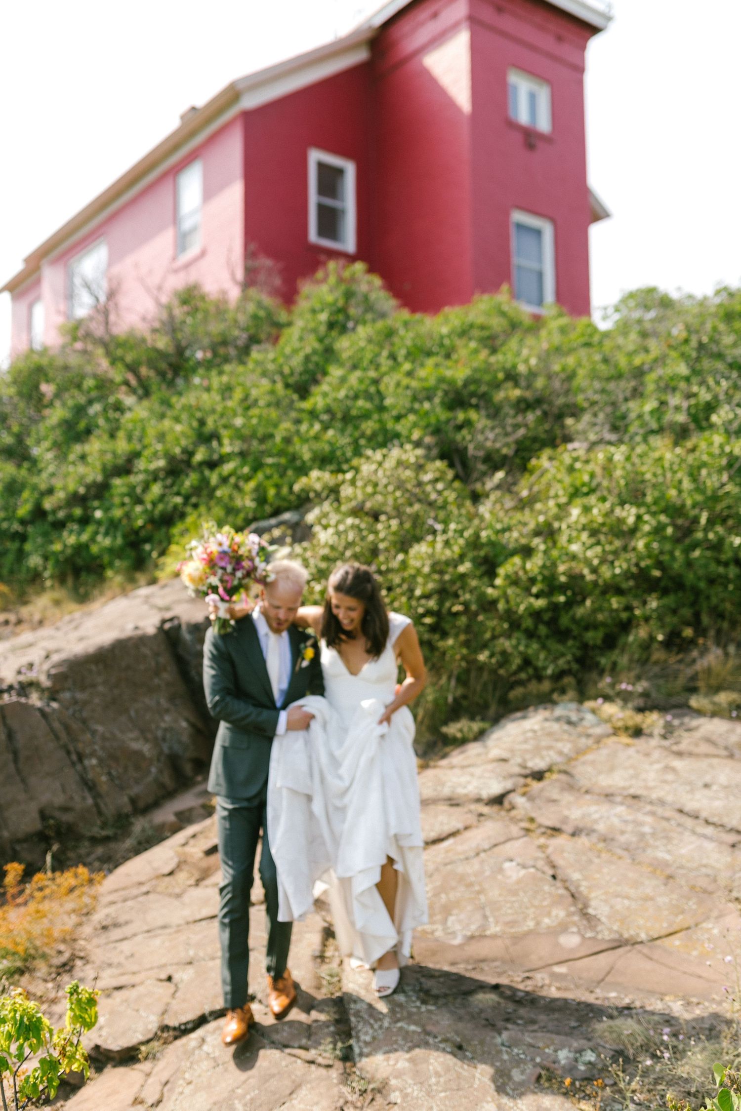 Couple walking along rocky terrain with pink and red buildings in the background.