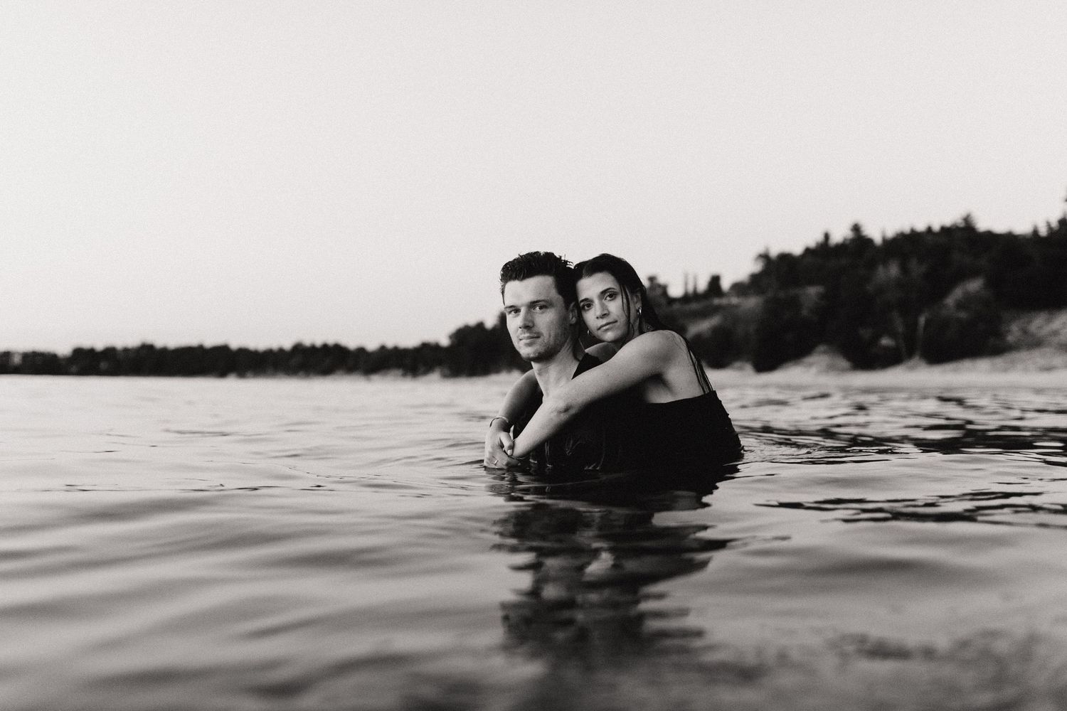 Black and white photo of a couple embracing in the ocean water near a sandy beach.