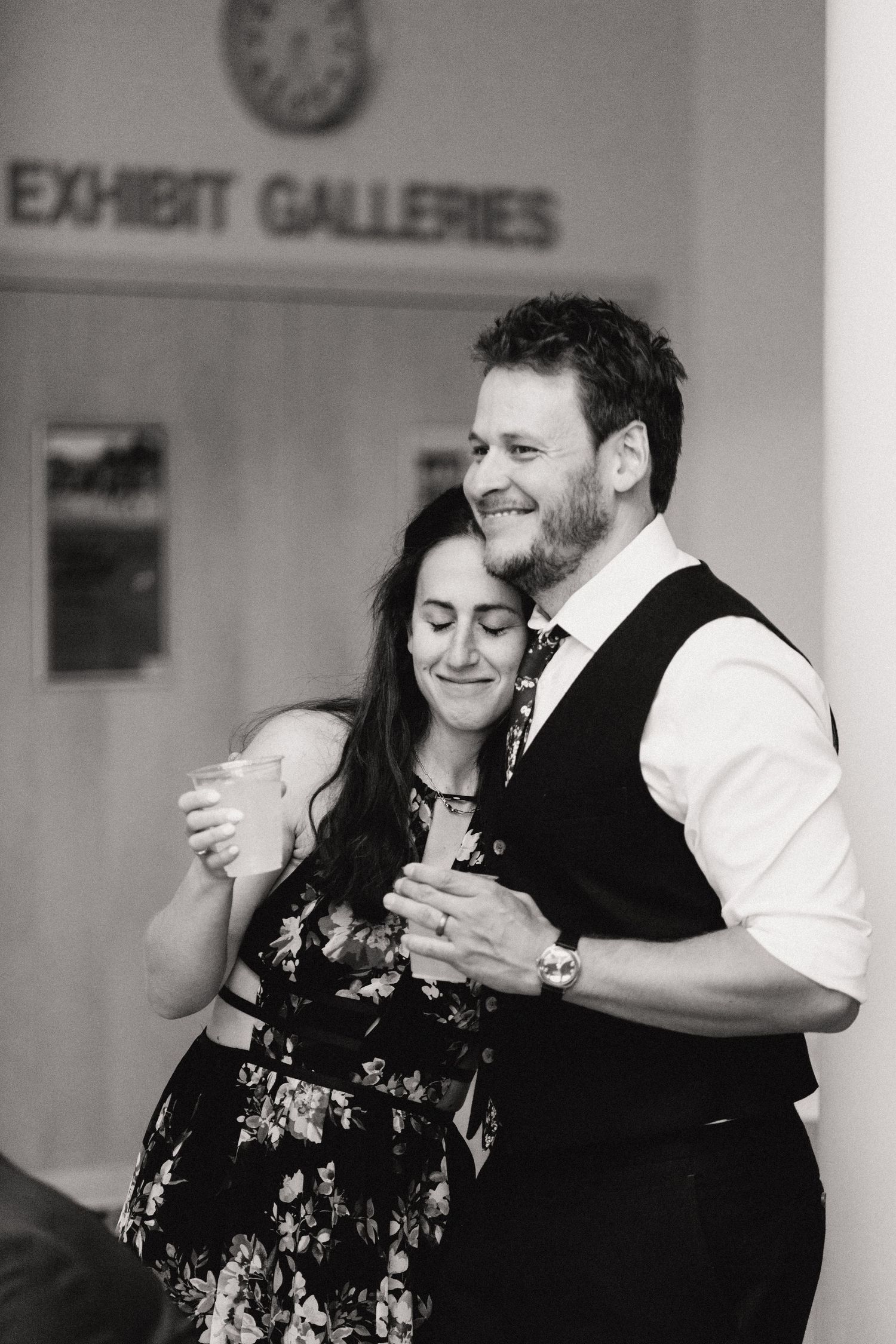 A romantic black and white photo of a couple dancing in formal attire at an indoor event.