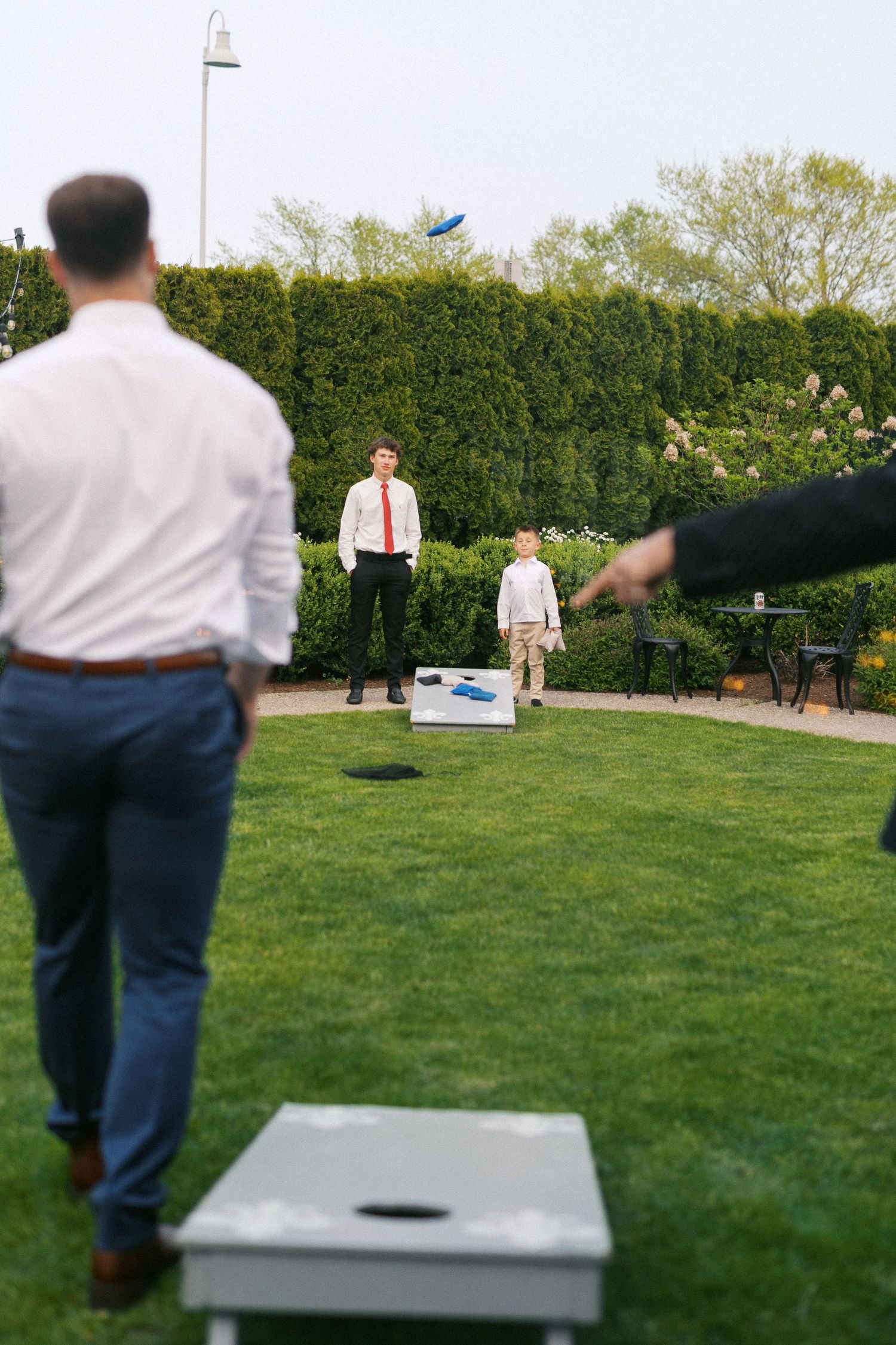 People playing cornhole on a grassy lawn with hedges in the background during an outdoor event.