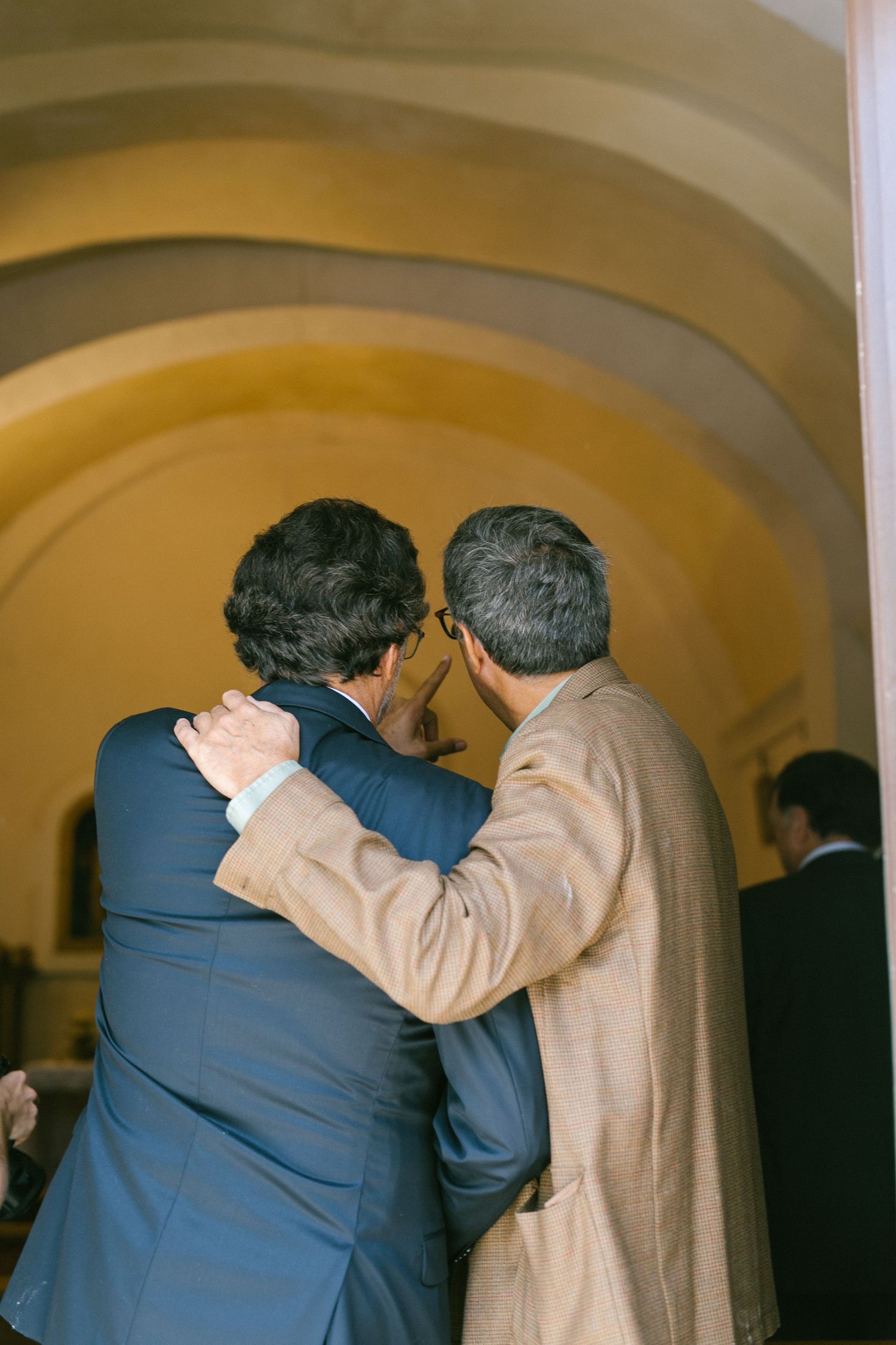 Two people embrace emotionally beneath an arched hallway during a wedding celebration.