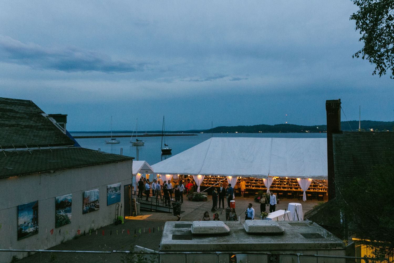 Panoramic view of a waterfront venue at dusk with string lights.