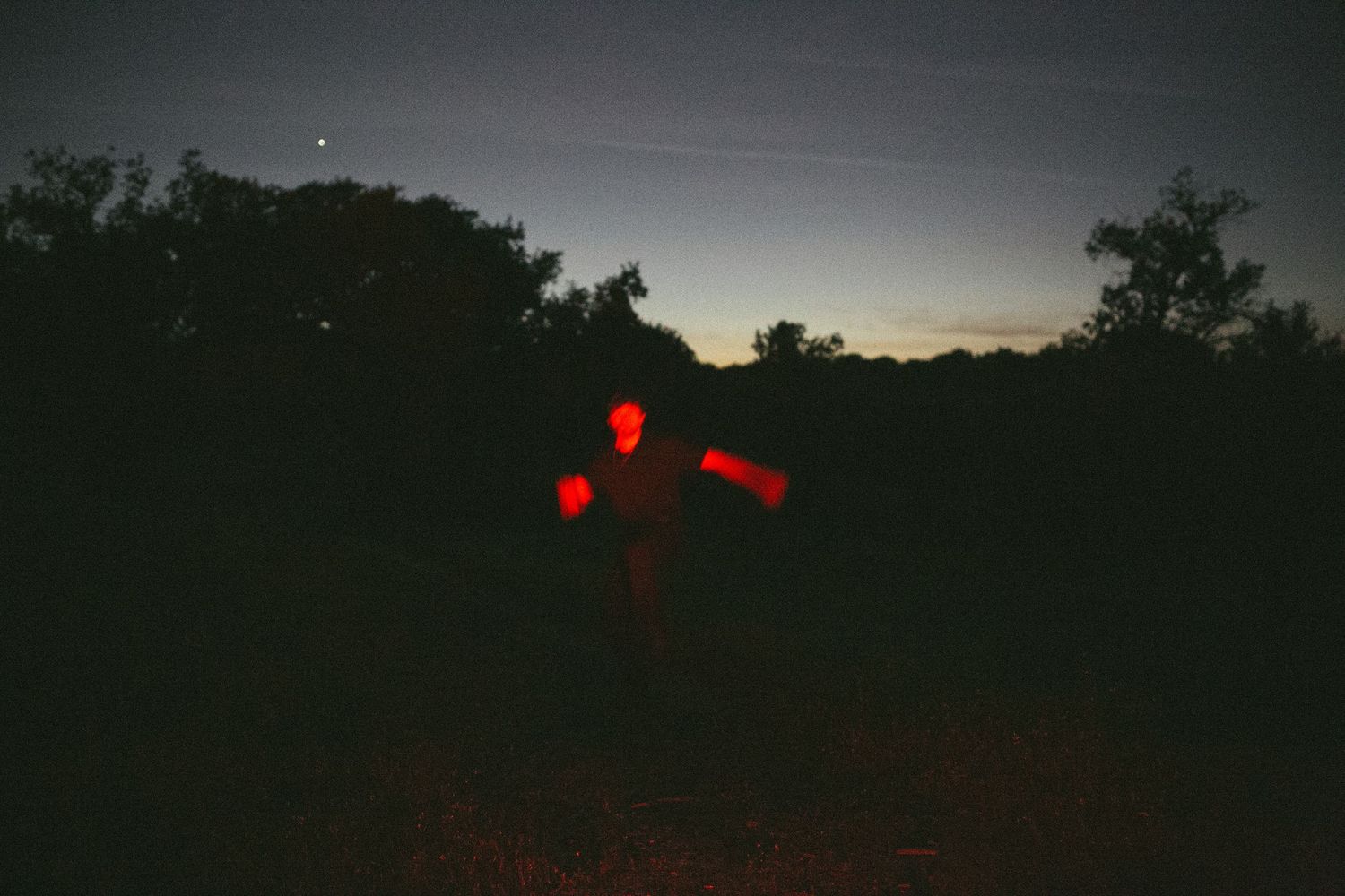 Person outlined in glowing red light standing in a dark field under a twilight sky.