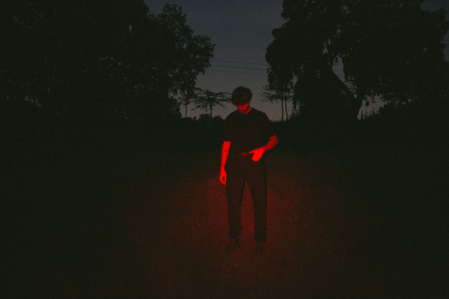 Dark atmospheric photo of a lone figure illuminated by red light in an outdoor night setting.