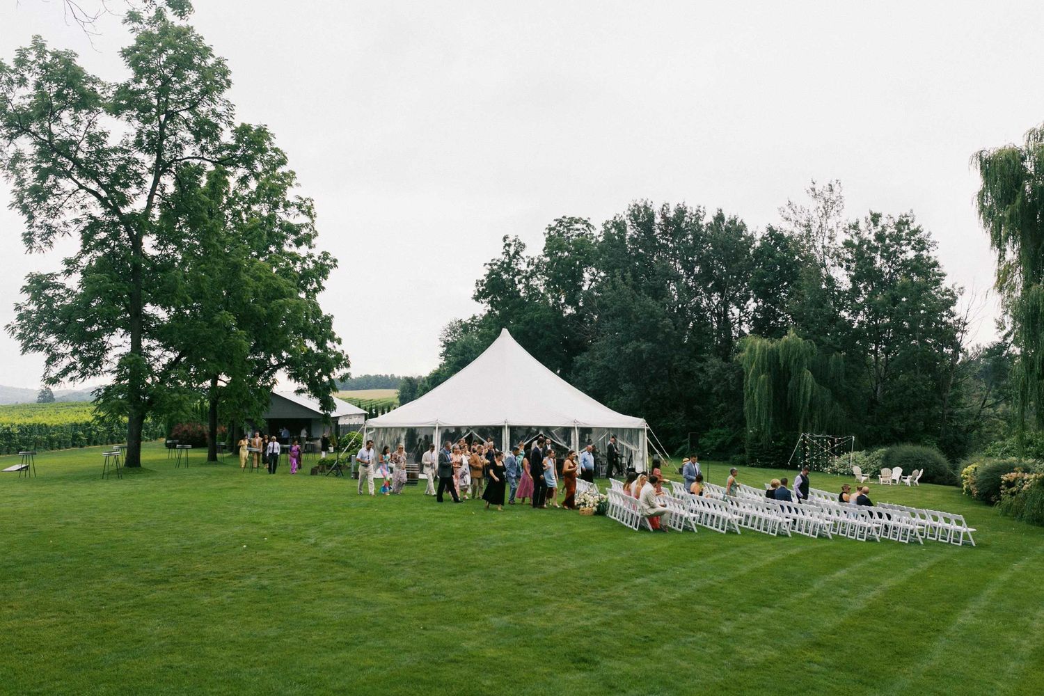 White wedding tent set up on a lush green lawn with trees in the background for an outdoor celebration.