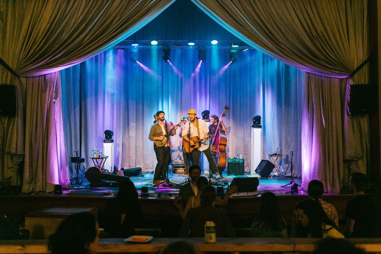 A live folk band performs on stage with colorful blue and purple stage lighting and elegant draped curtains in the background.