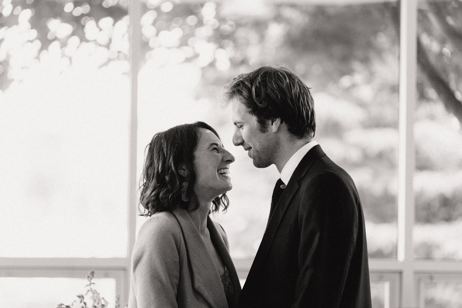 Black and white intimate portrait of a romantic couple about to kiss by a bright window.
