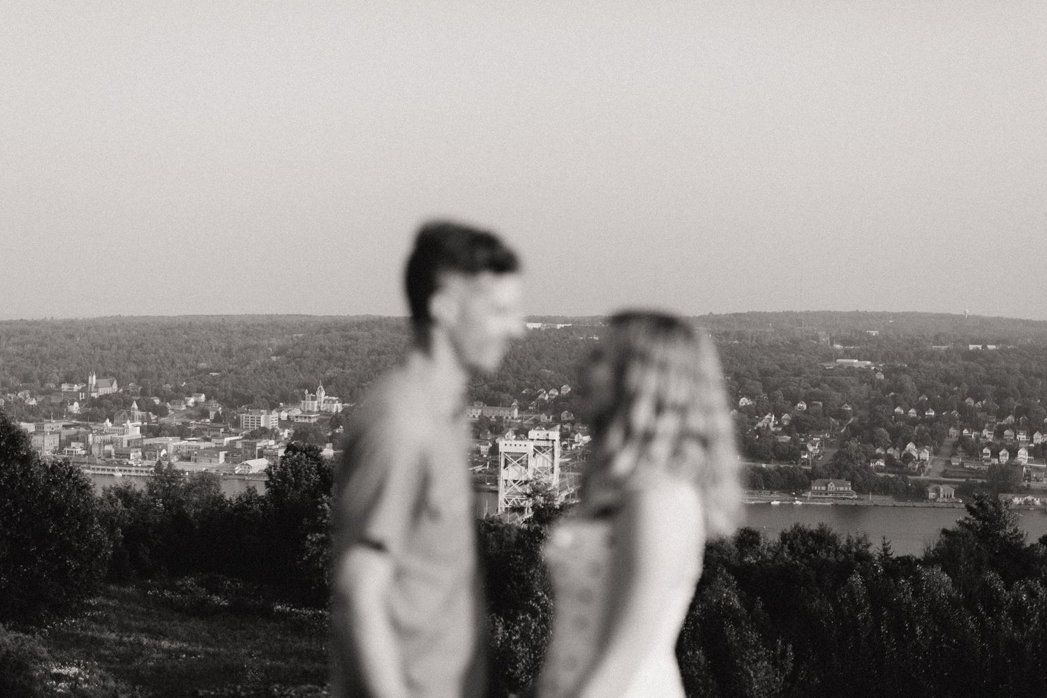 A black and white silhouette of a couple enjoying a scenic cityscape view from a hilltop.