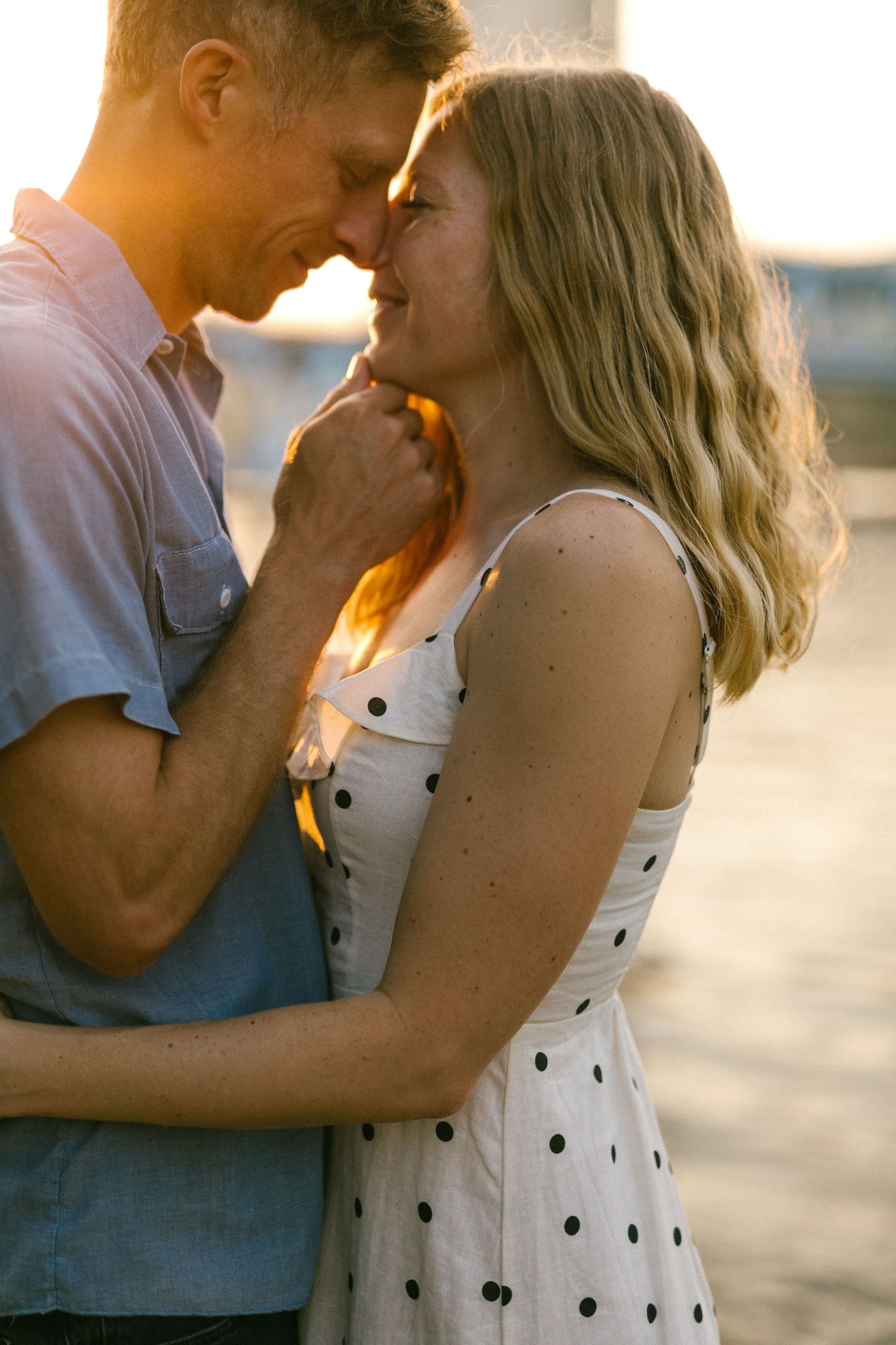 Couple sharing an intimate moment during golden hour with soft sunlight illuminating their faces.