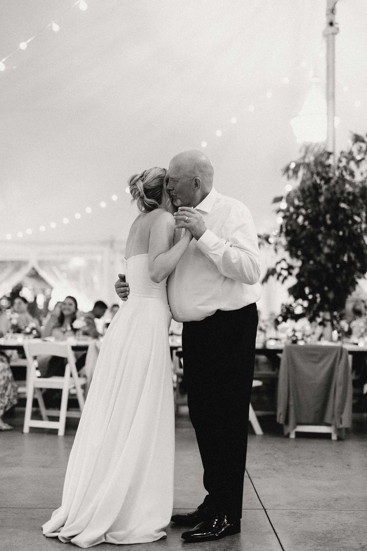 A romantic first dance sequence showing a couple swaying together under a wedding tent at an outdoor reception.