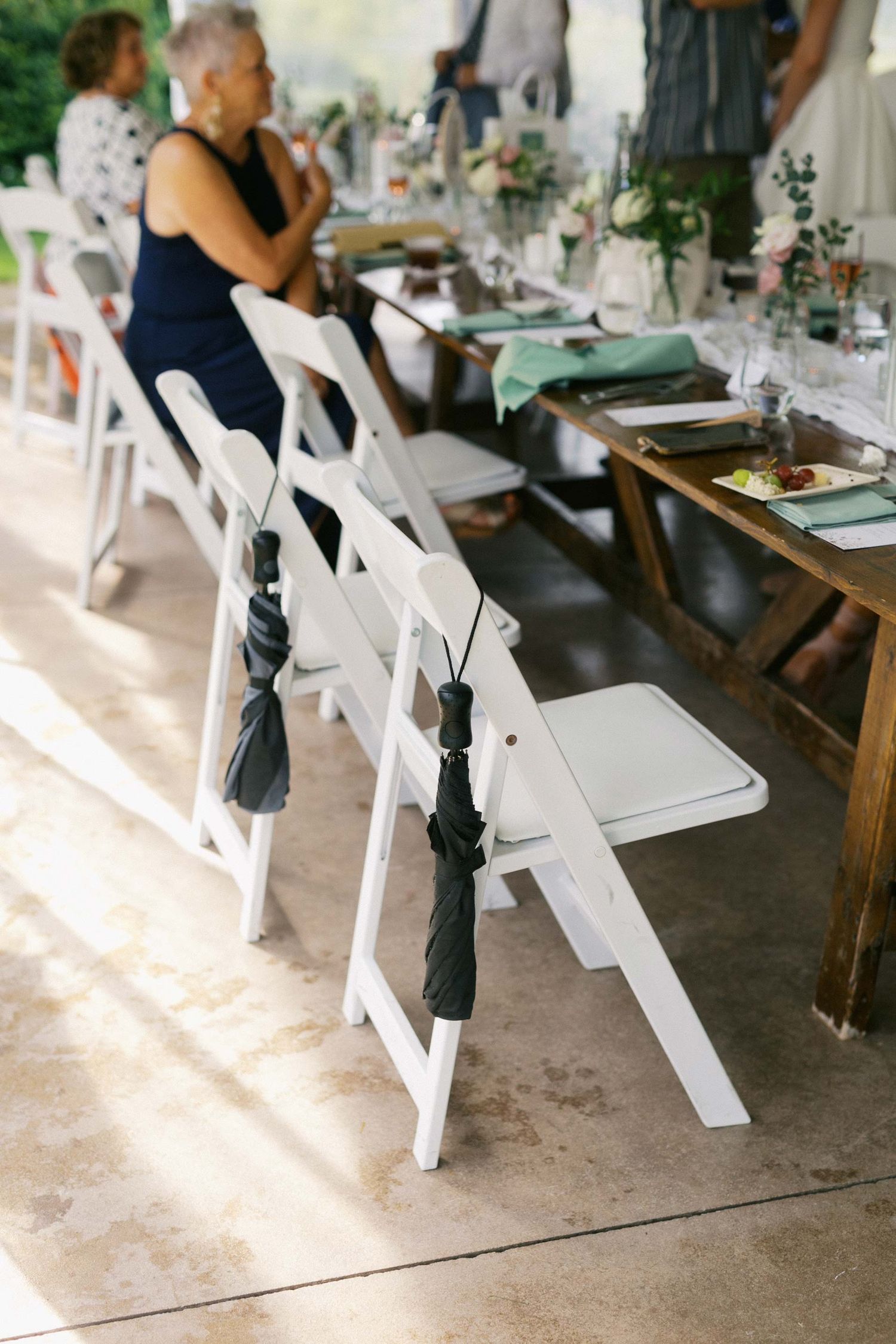 White wooden folding chairs arranged in rows at an outdoor wedding venue with concrete flooring and rustic decor.