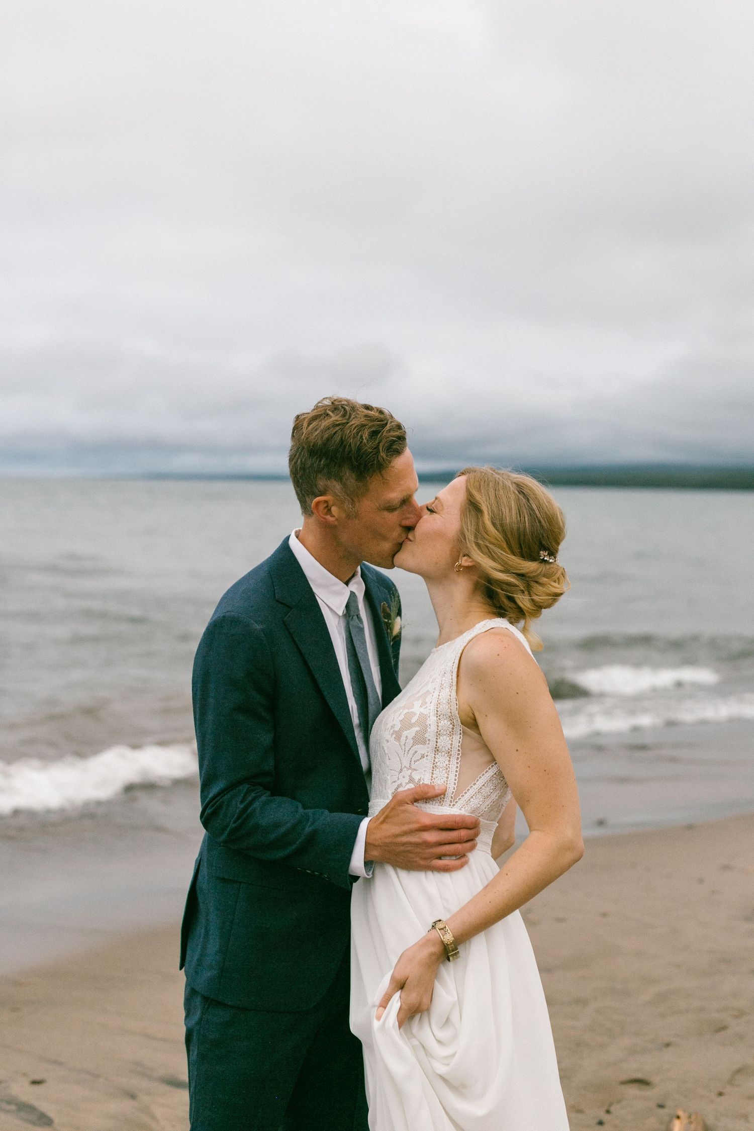 A romantic moment shared between two people on a windswept beach under cloudy skies.