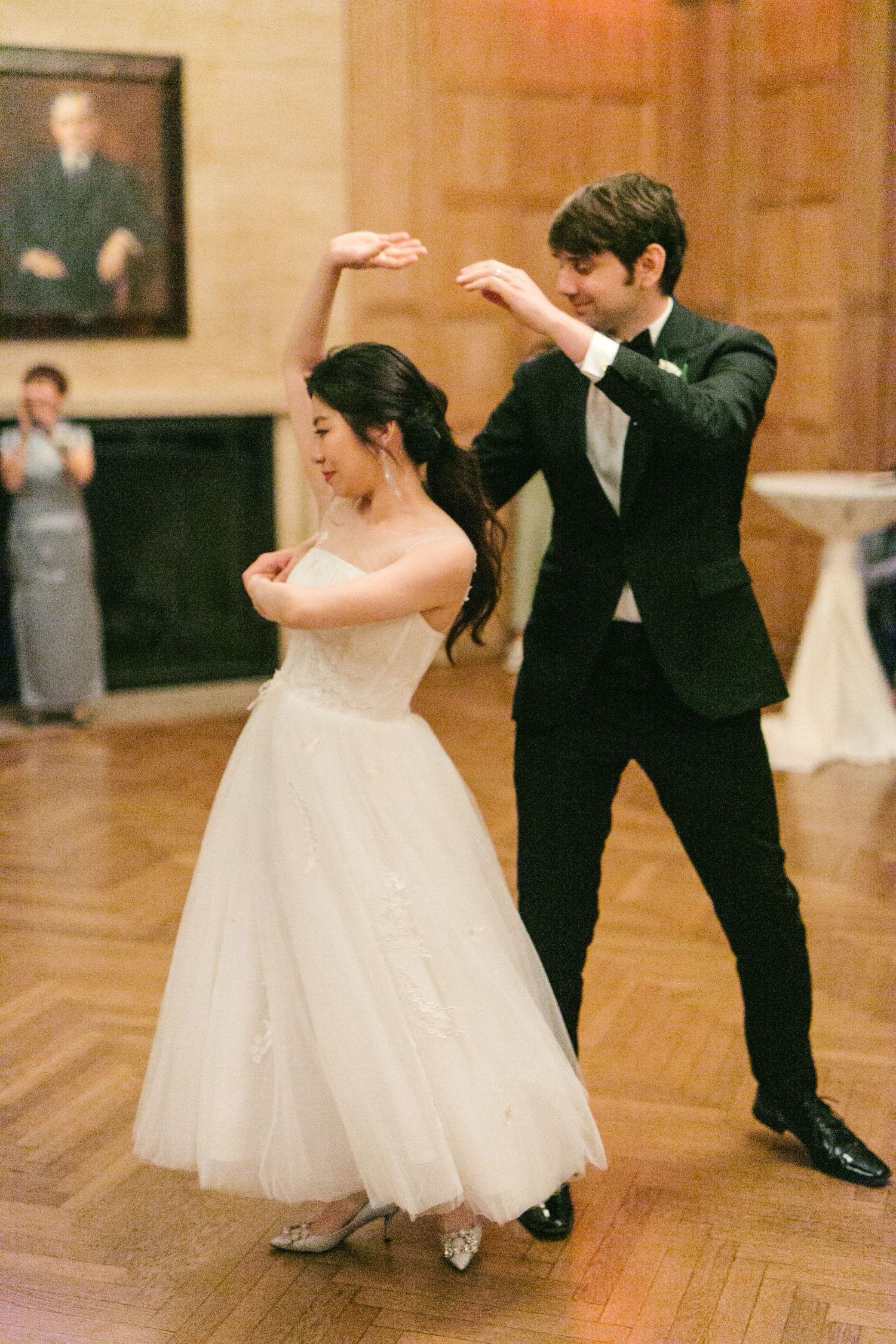 Bride and groom share joyful first dance, groom twirling bride in white ball gown on wooden dance floor.