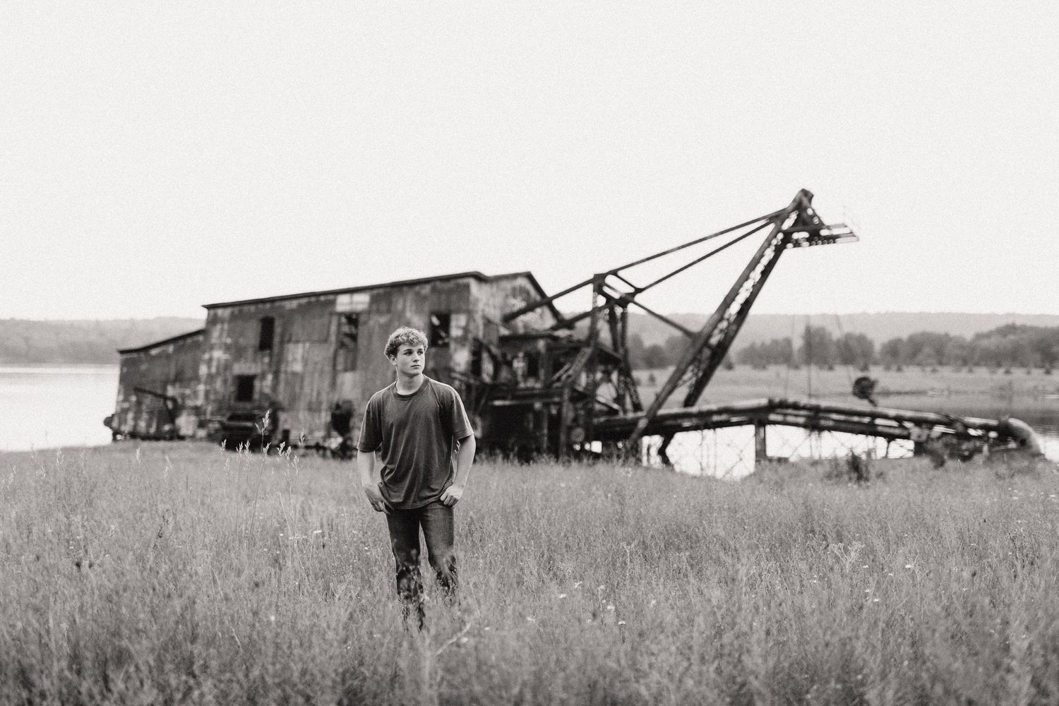 Black and white photo of boy standing in field near abandoned machinery.
