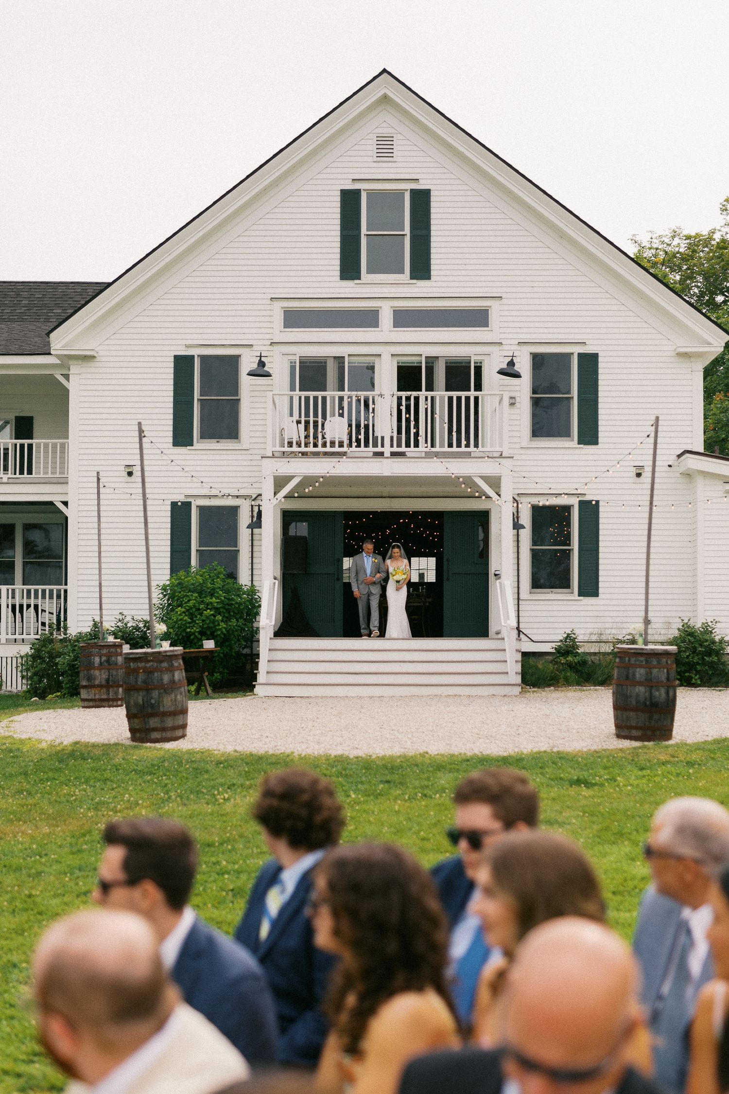 A bride walks down the aisle at an outdoor wedding ceremony in front of a white Inn venue.