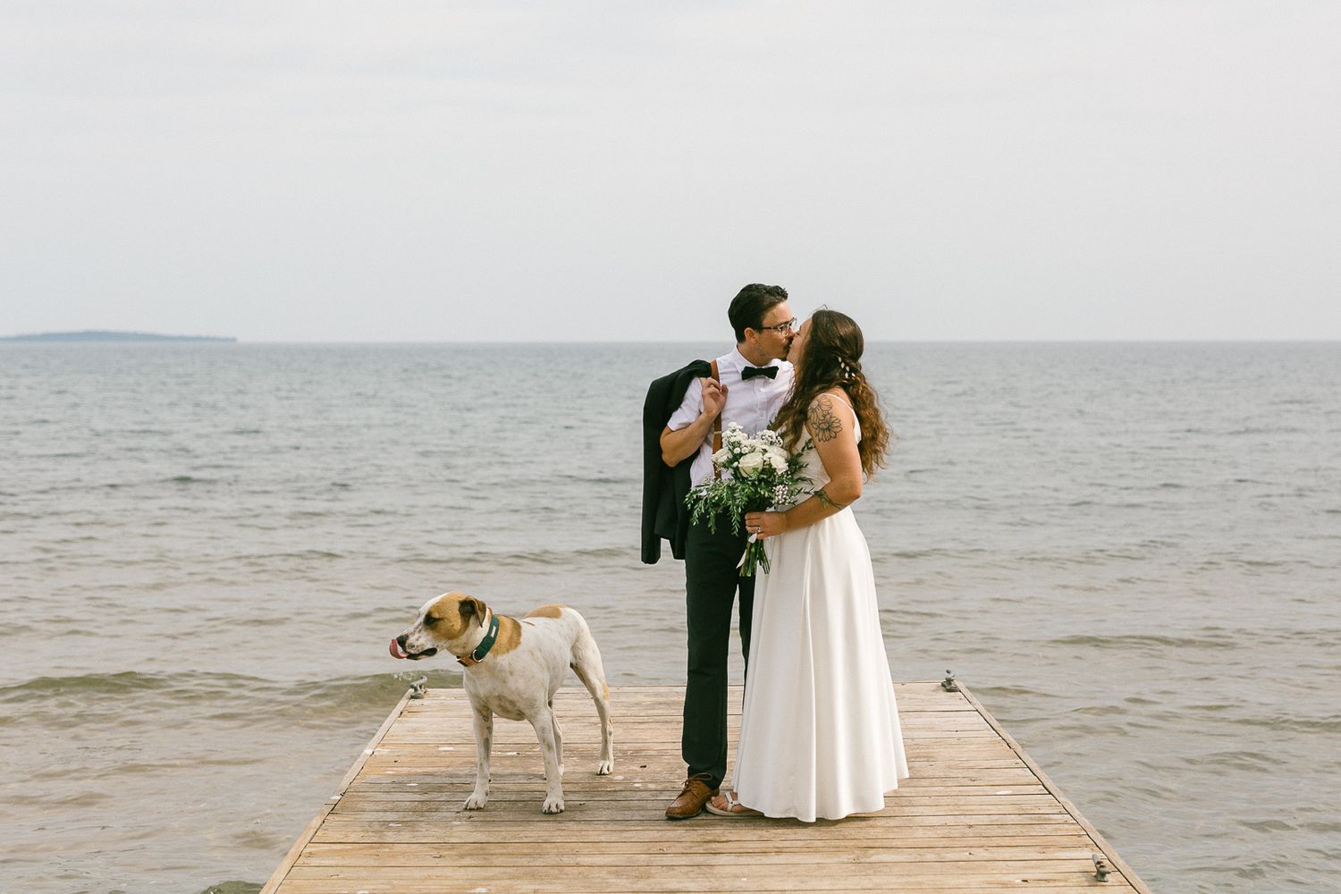 Romantic waterfront wedding scene with a dog joining the couple on a dock.