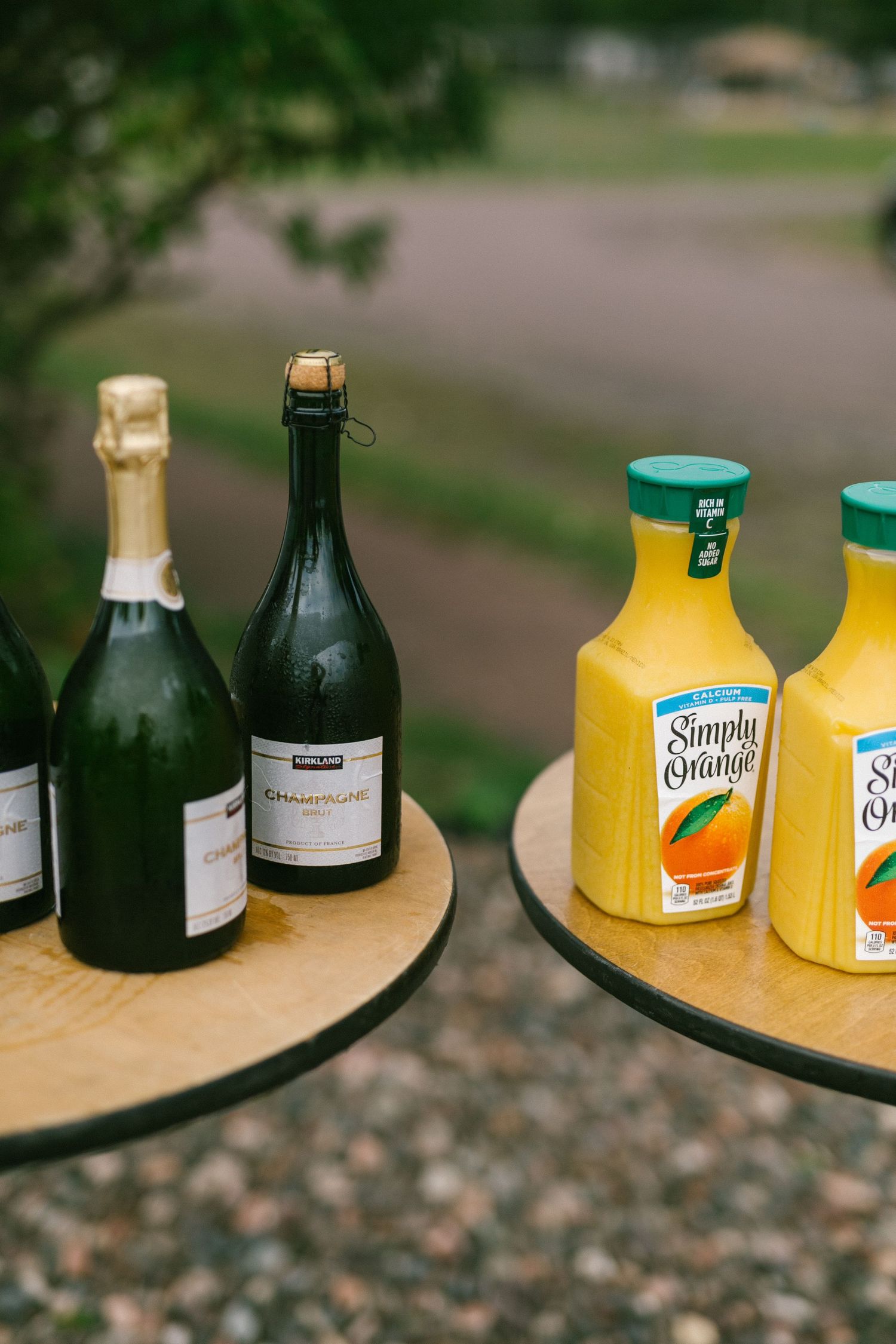 Bottles of champagne and Simply Orange juice displayed on round serving trays outdoors for a brunch setup.