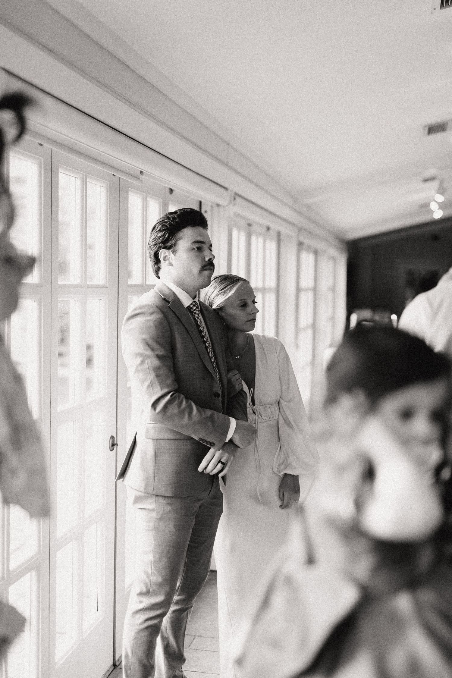 Wedding guests celebrate during a reception in a bright venue with large windows.