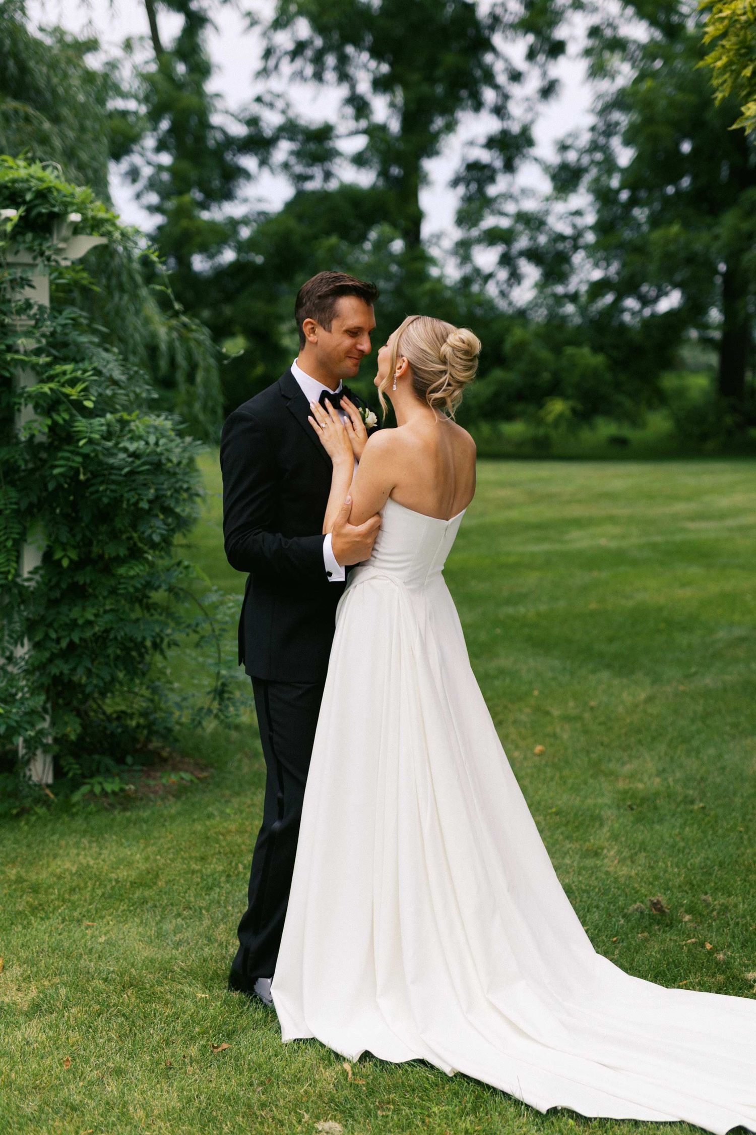 A bride and groom share an intimate moment outdoors on their wedding day in a lush green garden setting.