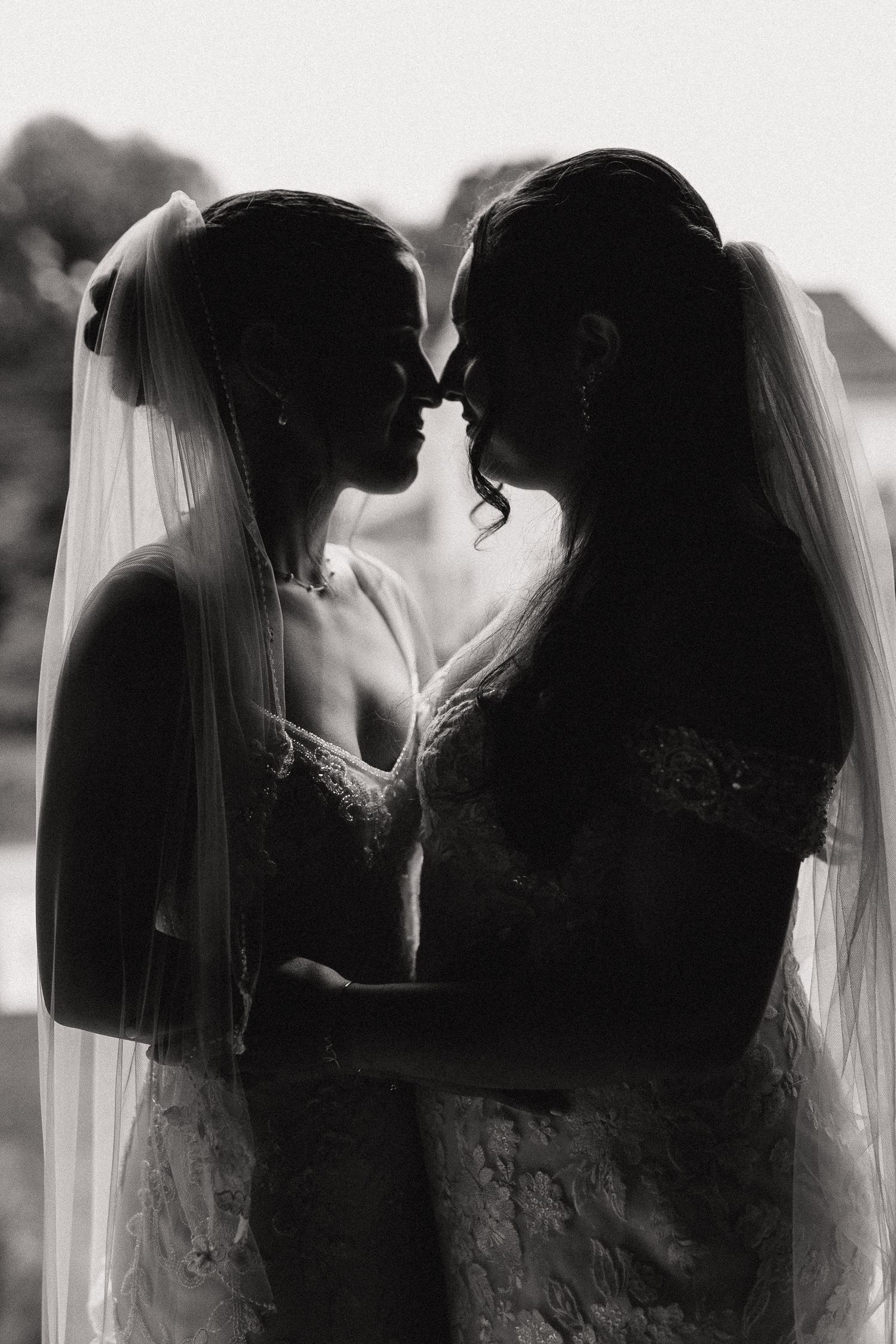 Black and white silhouette of two brides in wedding dresses and veils sharing an intimate moment.