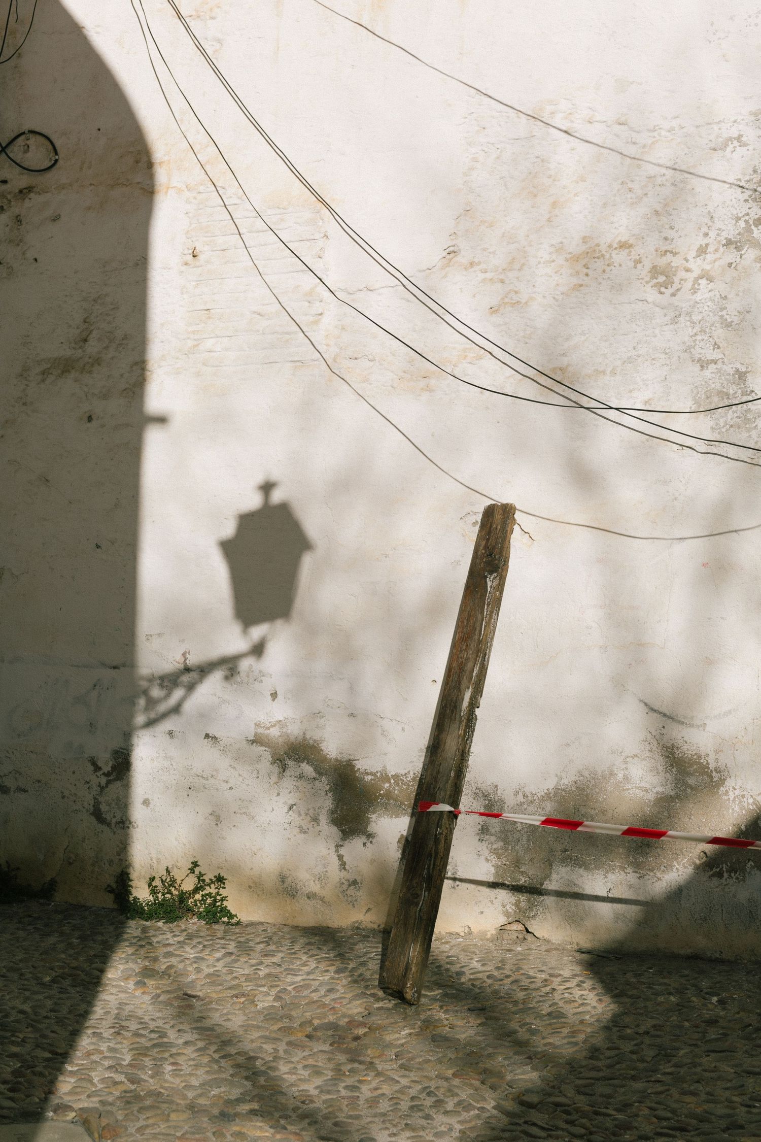 Shadow of a street lamp cast on a white wall with hanging electrical wires and a wooden post.