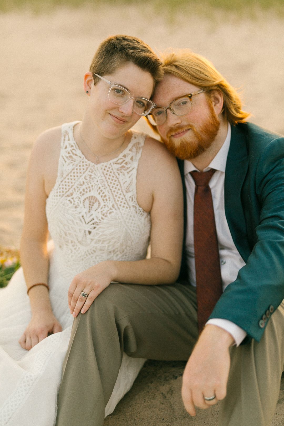A tender moment between a couple sitting on sand during their beach engagement session.