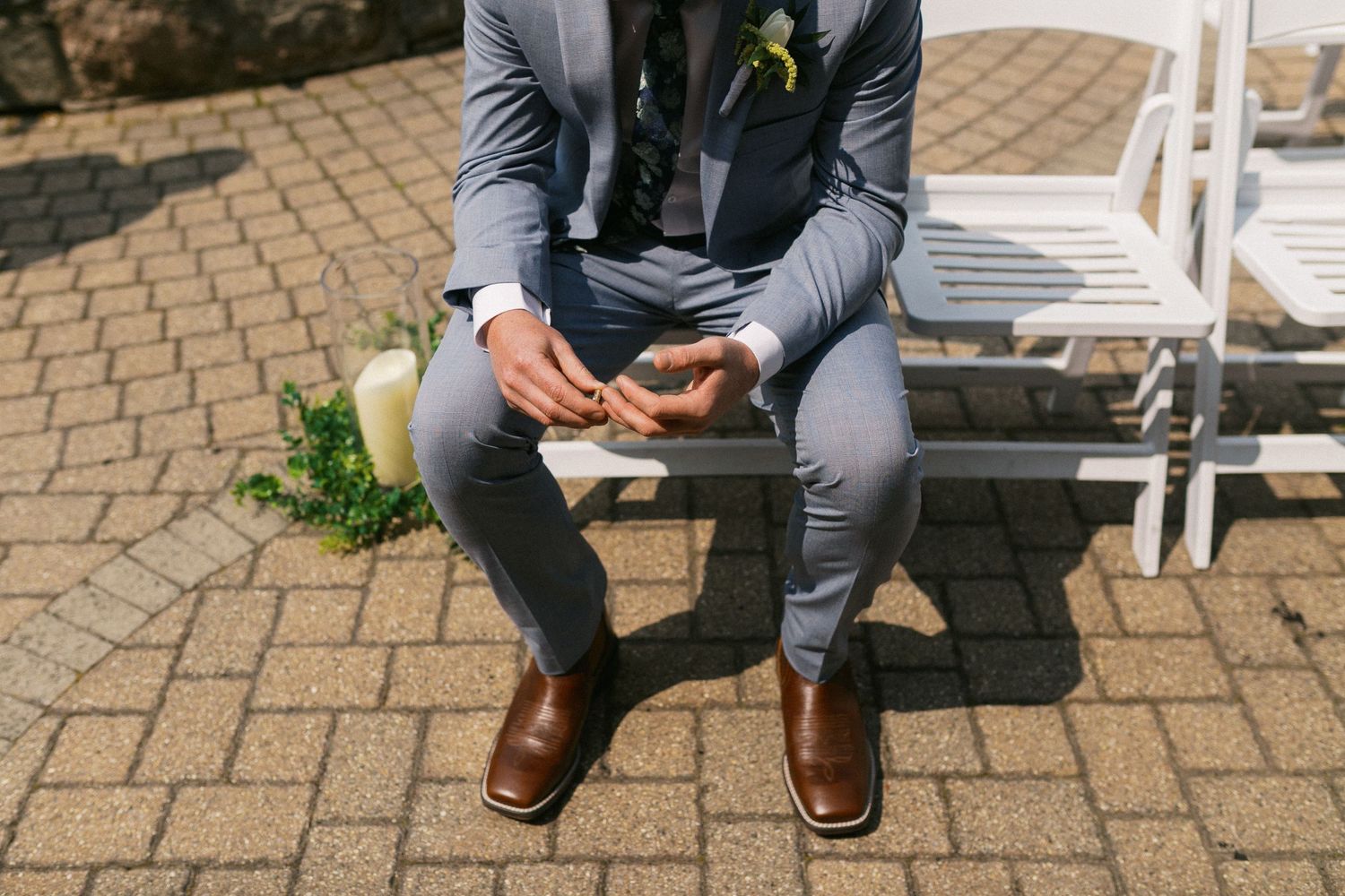 Close-up detail shot of groom's formal attire and shoes while seated on brick pavers.