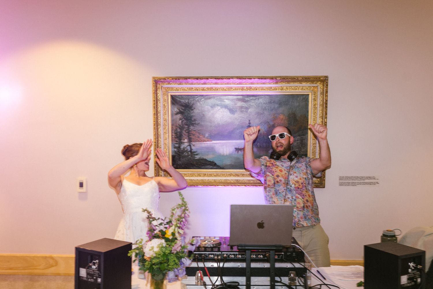 DJs at a party work together behind the decks with a decorative painting and sound equipment.