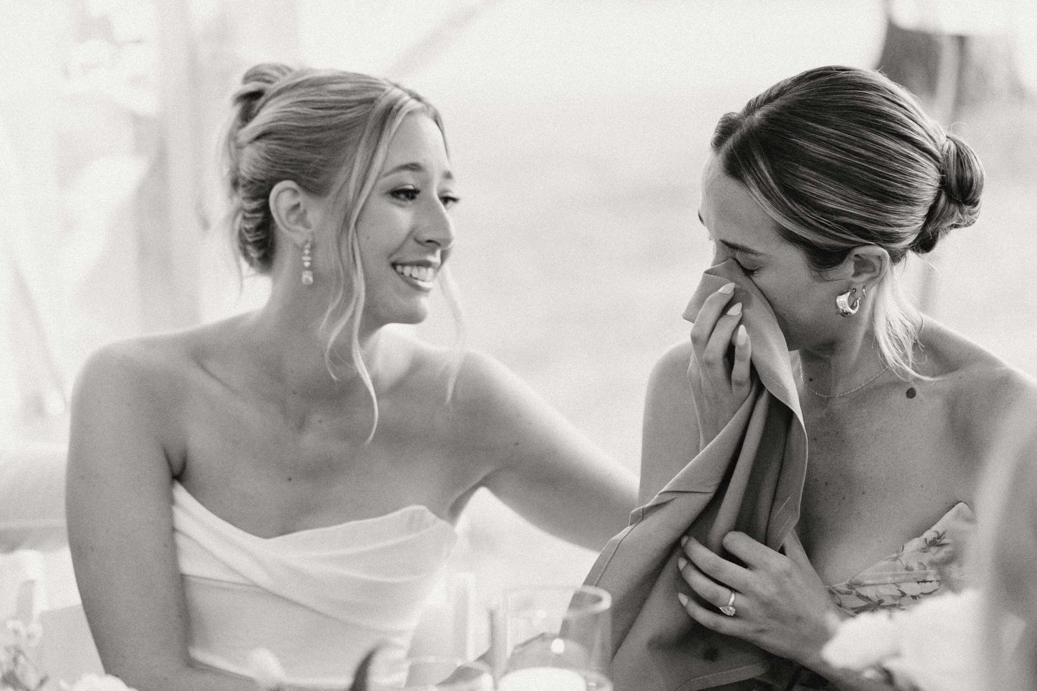 A heartwarming black and white photograph capturing a candid moment of shared laughter at a wedding celebration.