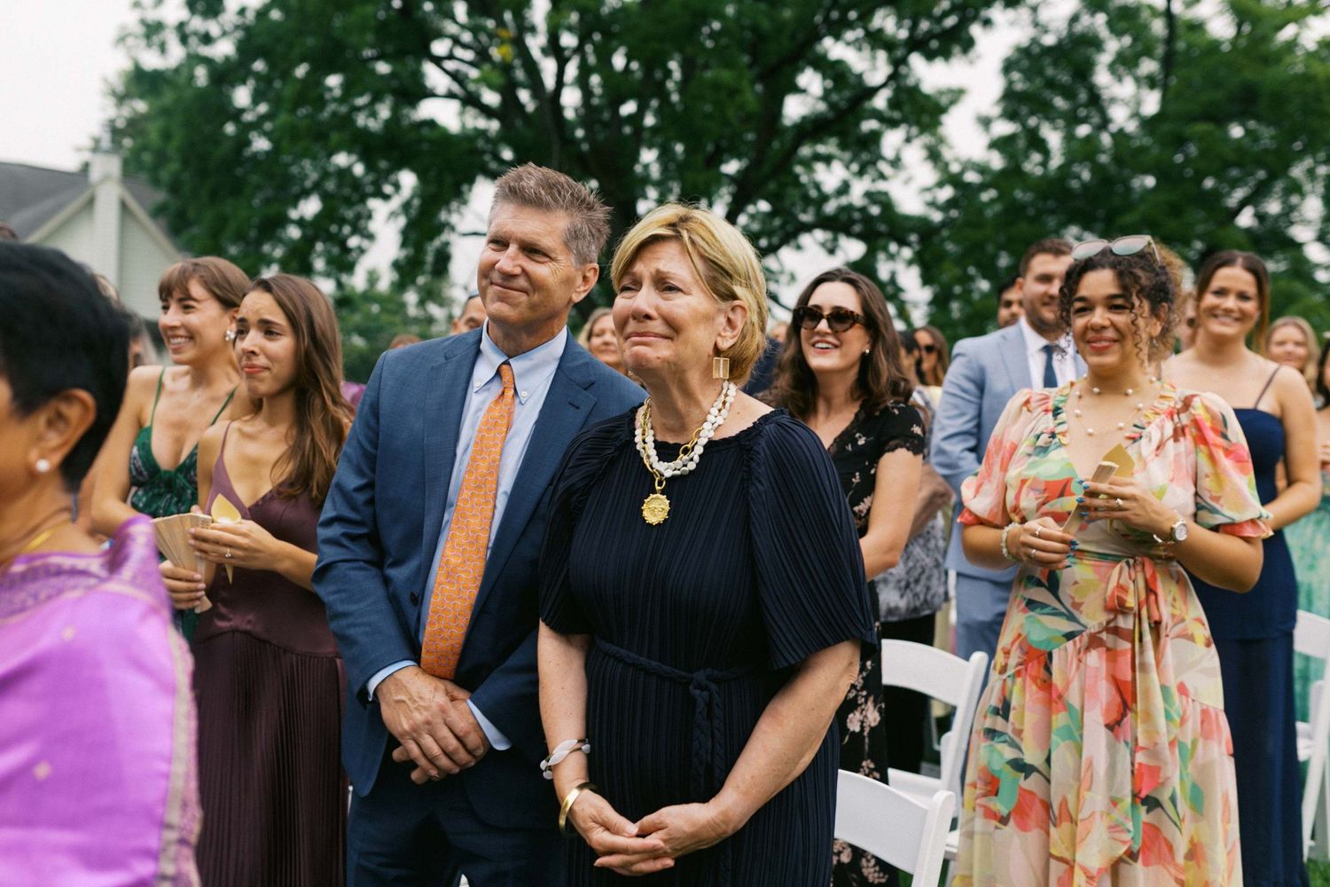 Wedding guests gather outdoors at a celebration event, smiling and mingling in formal attire.