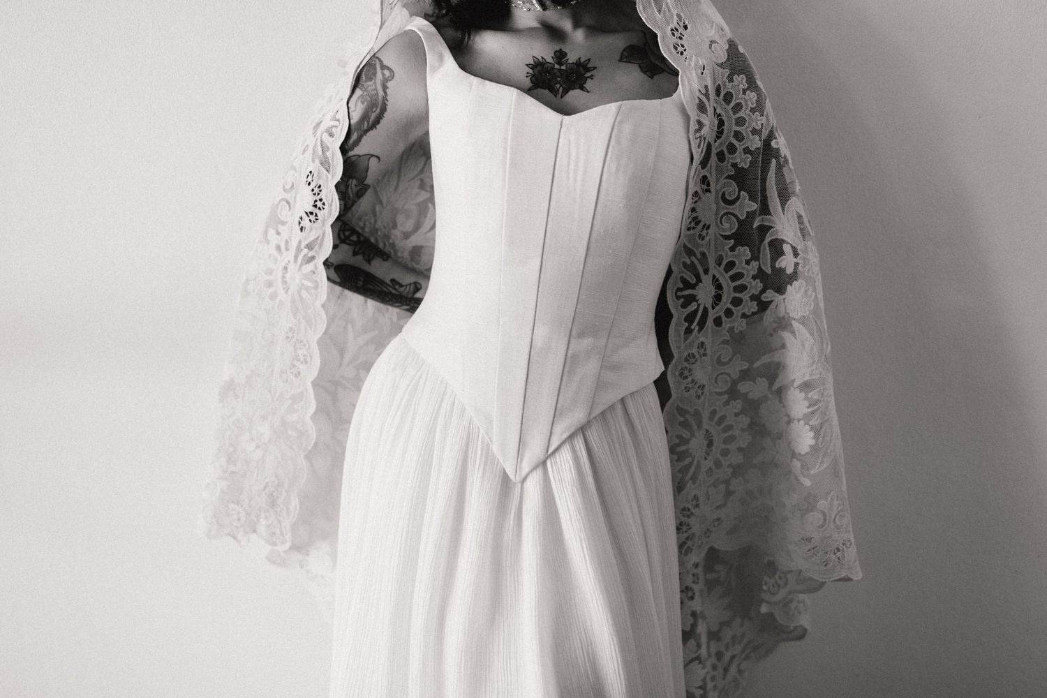 Black and white photo of a bride in a corset wedding dress with lace veil and tattoos.