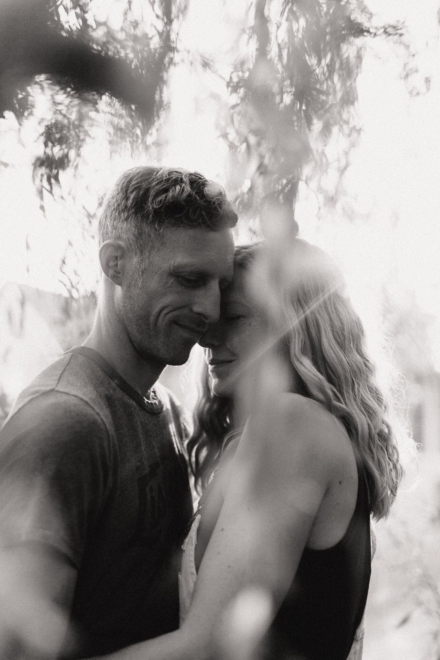 Intimate black and white portrait of a couple sharing a tender moment outdoors.