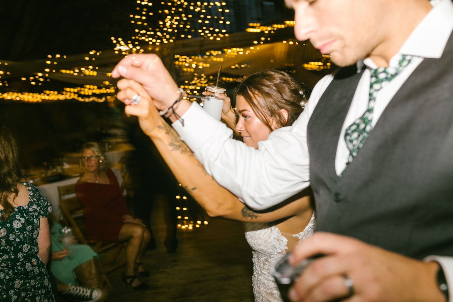 Wedding guests dancing enthusiastically at an evening reception with golden lights in the background.