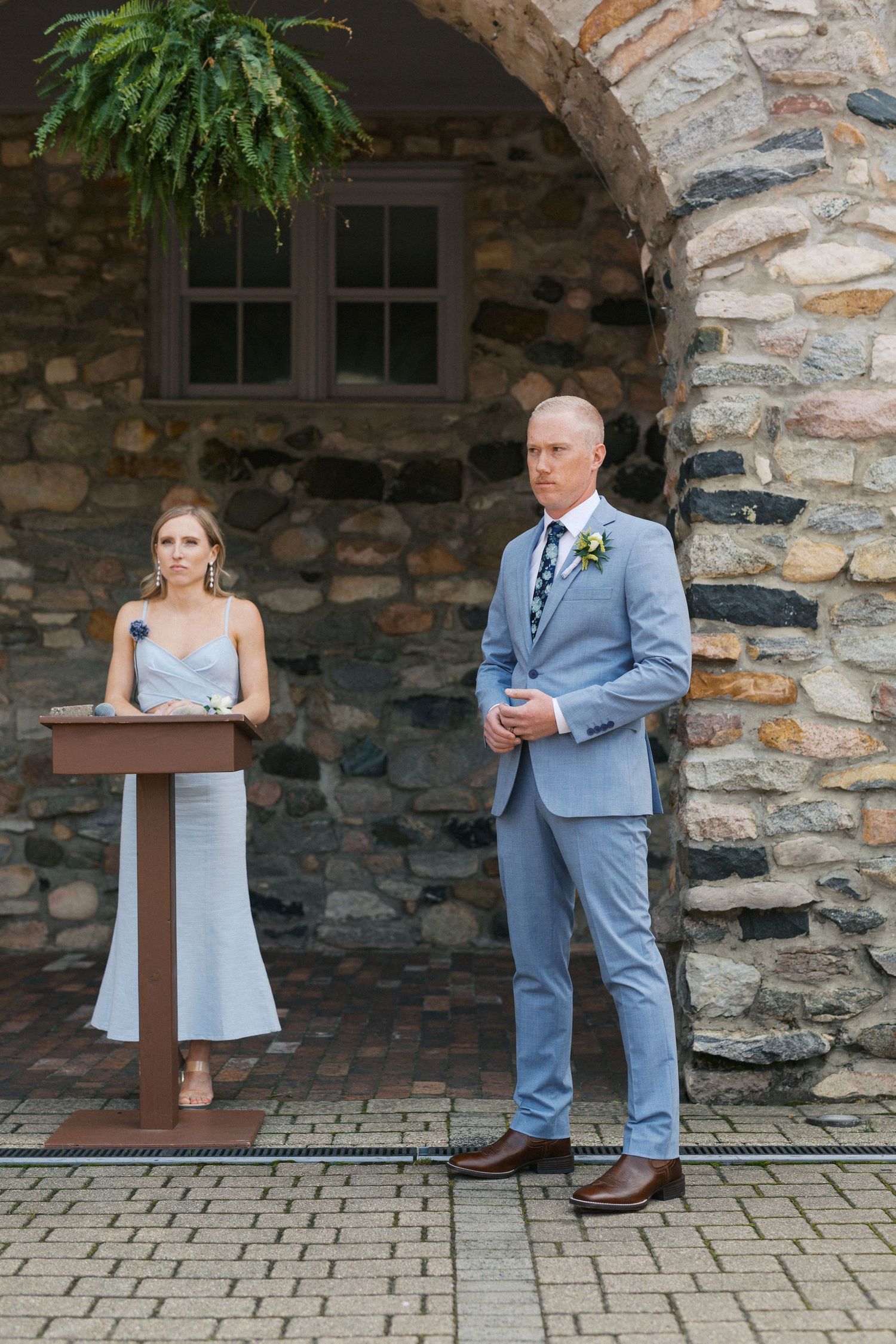 Wedding party members in blue and gray attire standing against a rustic stone wall backdrop.