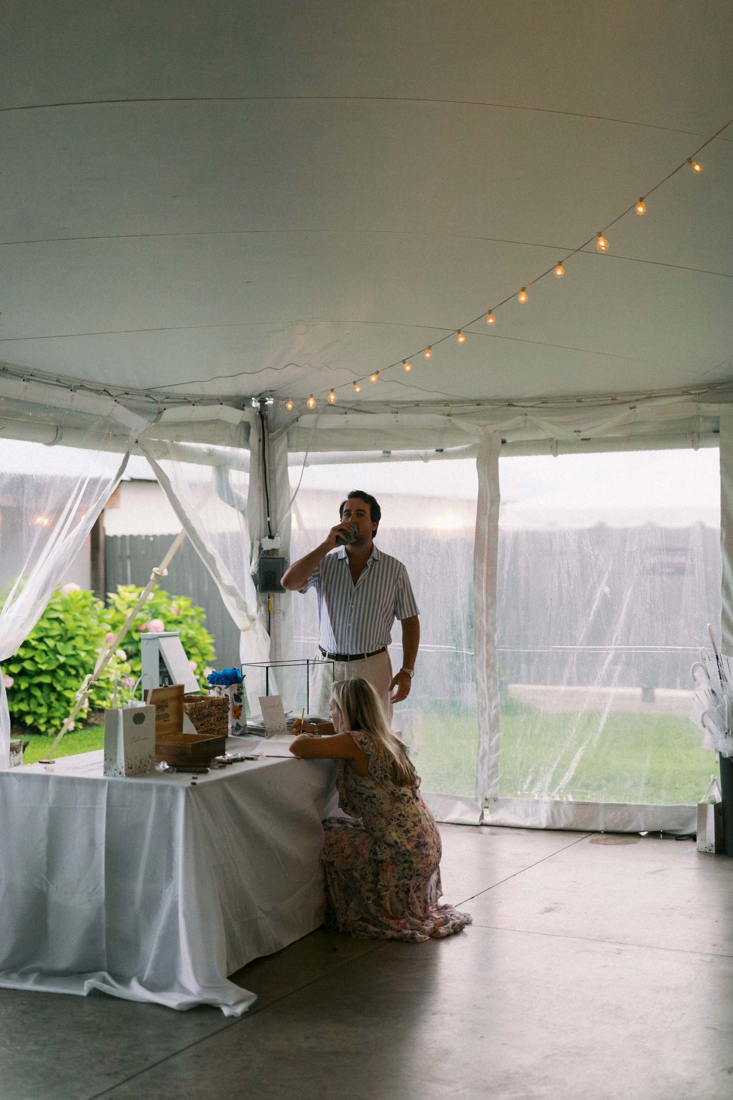 A couple dances together in an elegant white tent decorated with string lights and white tablecloths.