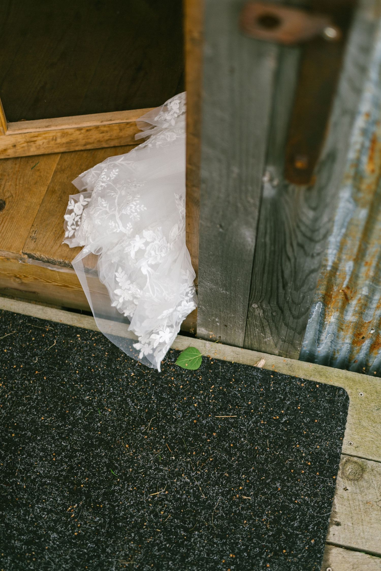 White wedding dress lace detail spills onto a dark doormat against rustic wooden floorboards.